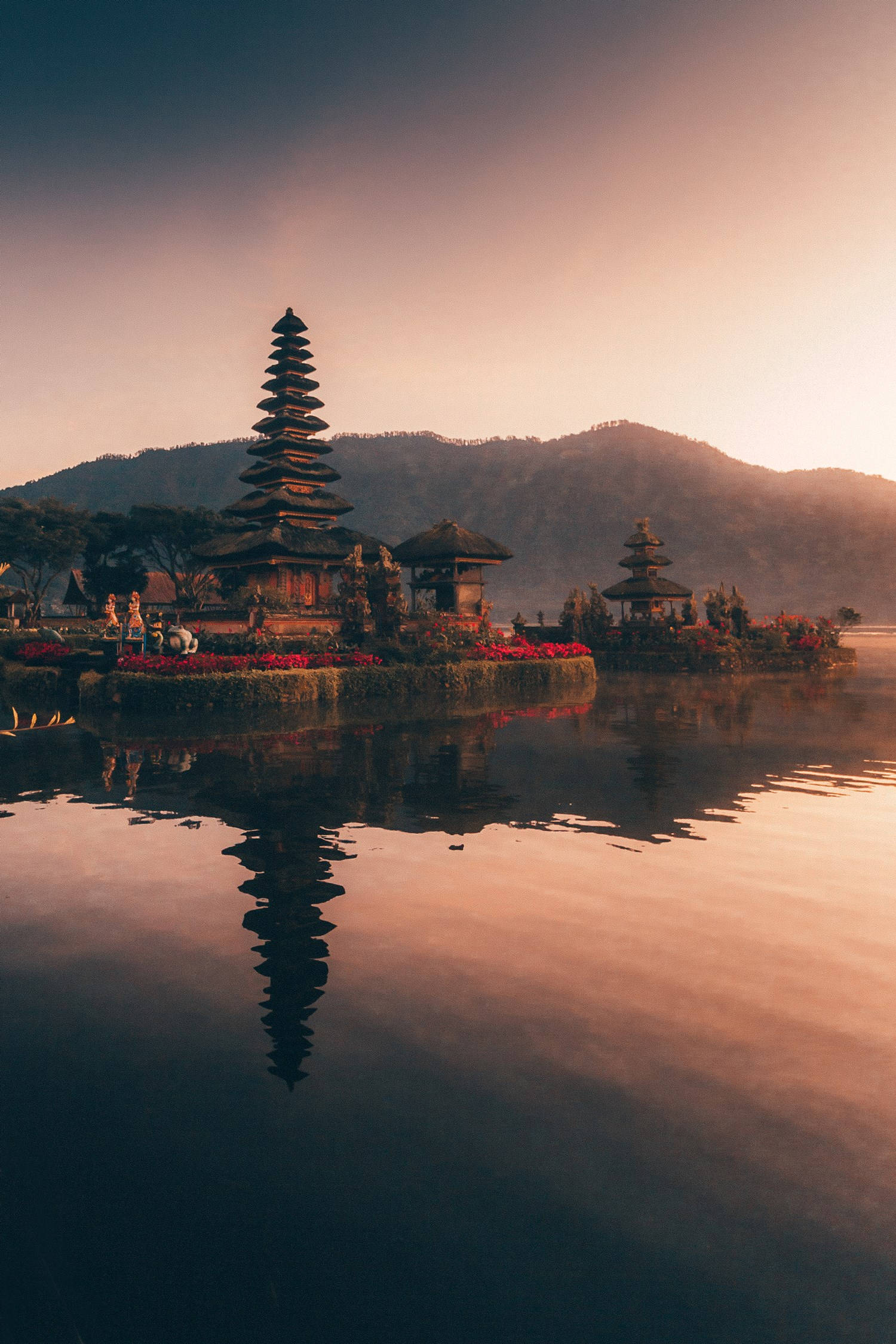 Vacation 桌布 壁紙 — 一個寧靜的峇里島寺廟群在日出時完美地倒映在平靜的水面上，背景是霧氣繚繞的山巒。