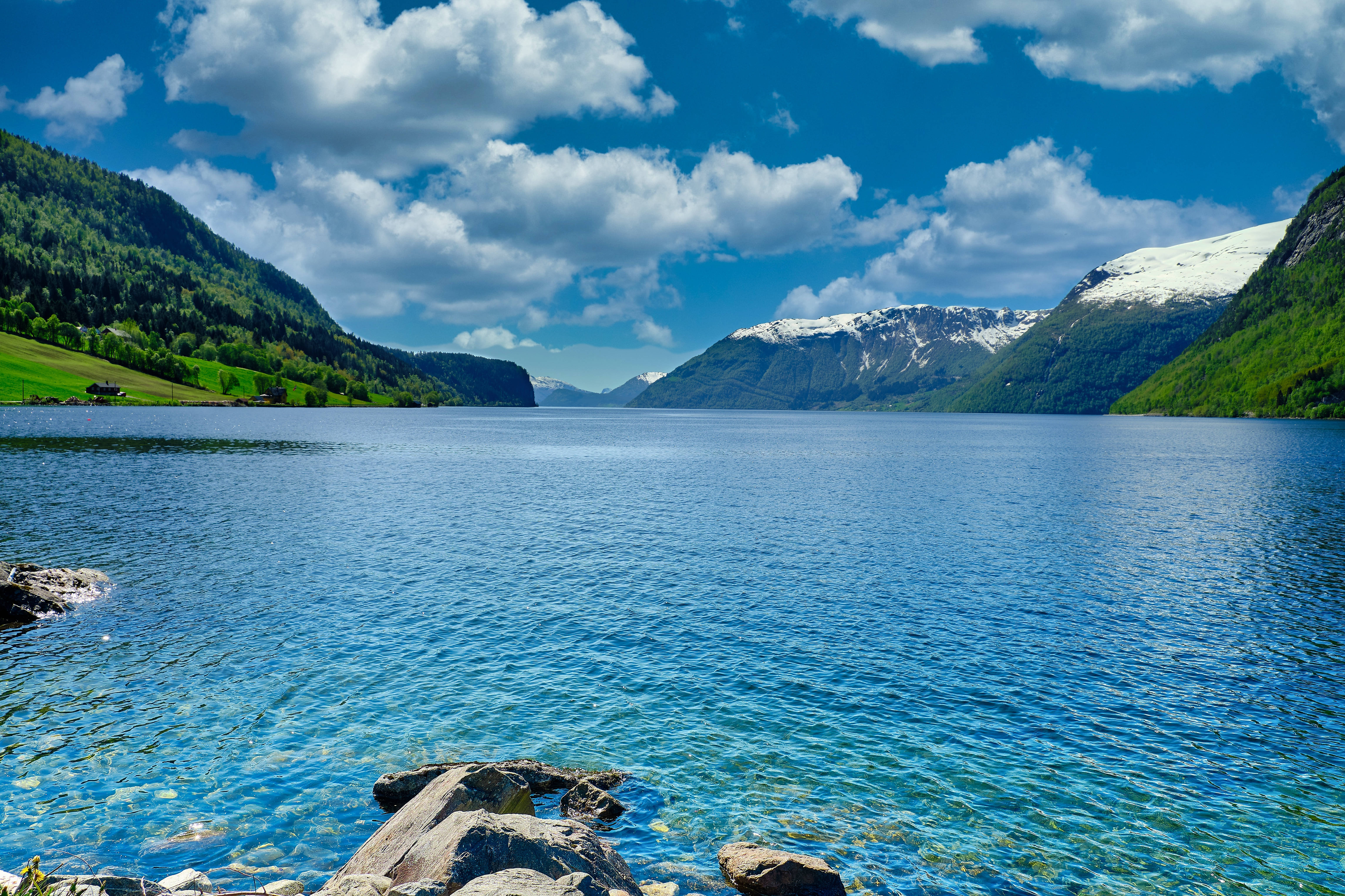 Lake 桌布 壁紙 — 一個寧靜的峽灣，碧綠的海水被鬱鬱蔥蔥的綠色山丘和白雪皚皚的山脈環繞，上方是明亮的藍天和蓬鬆的白雲。