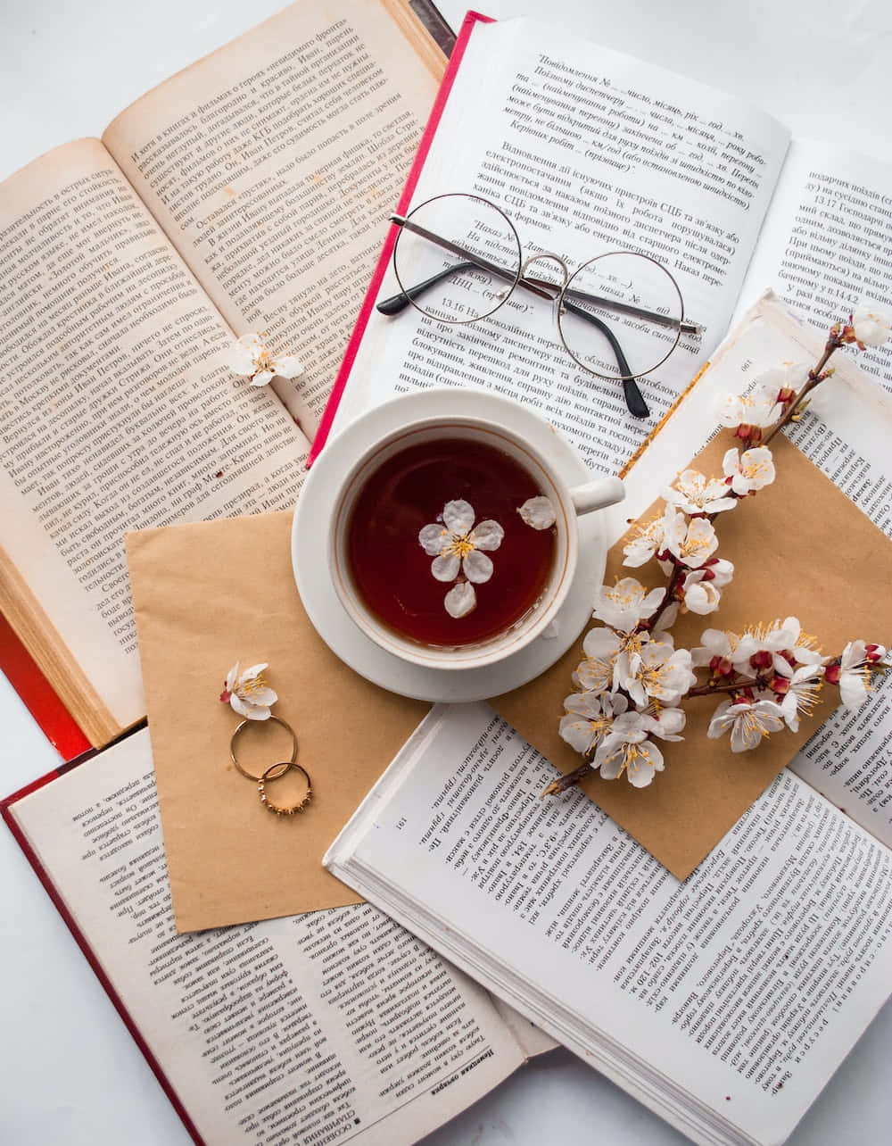 Floral Tea 桌布 壁紙 — 一個寧靜的平鋪構圖，包含打開的書本、眼鏡、茶、櫻花和戒指，置於白色表面上。