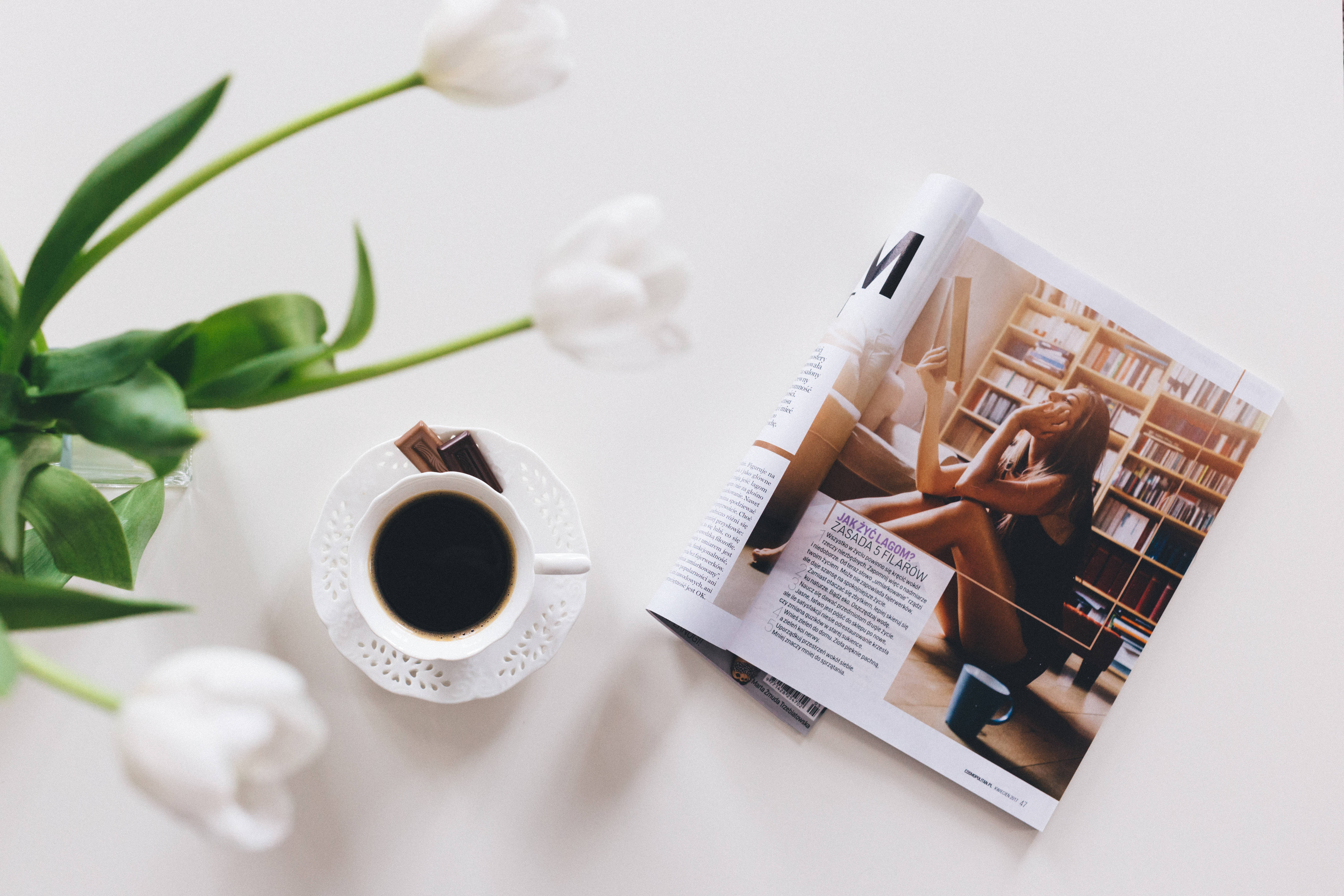 Magazine 桌布 壁紙 — 一個寧靜的平鋪構圖，包含白色鬱金香、一杯黑咖啡和一本打開的雜誌，放在潔白的表面上。