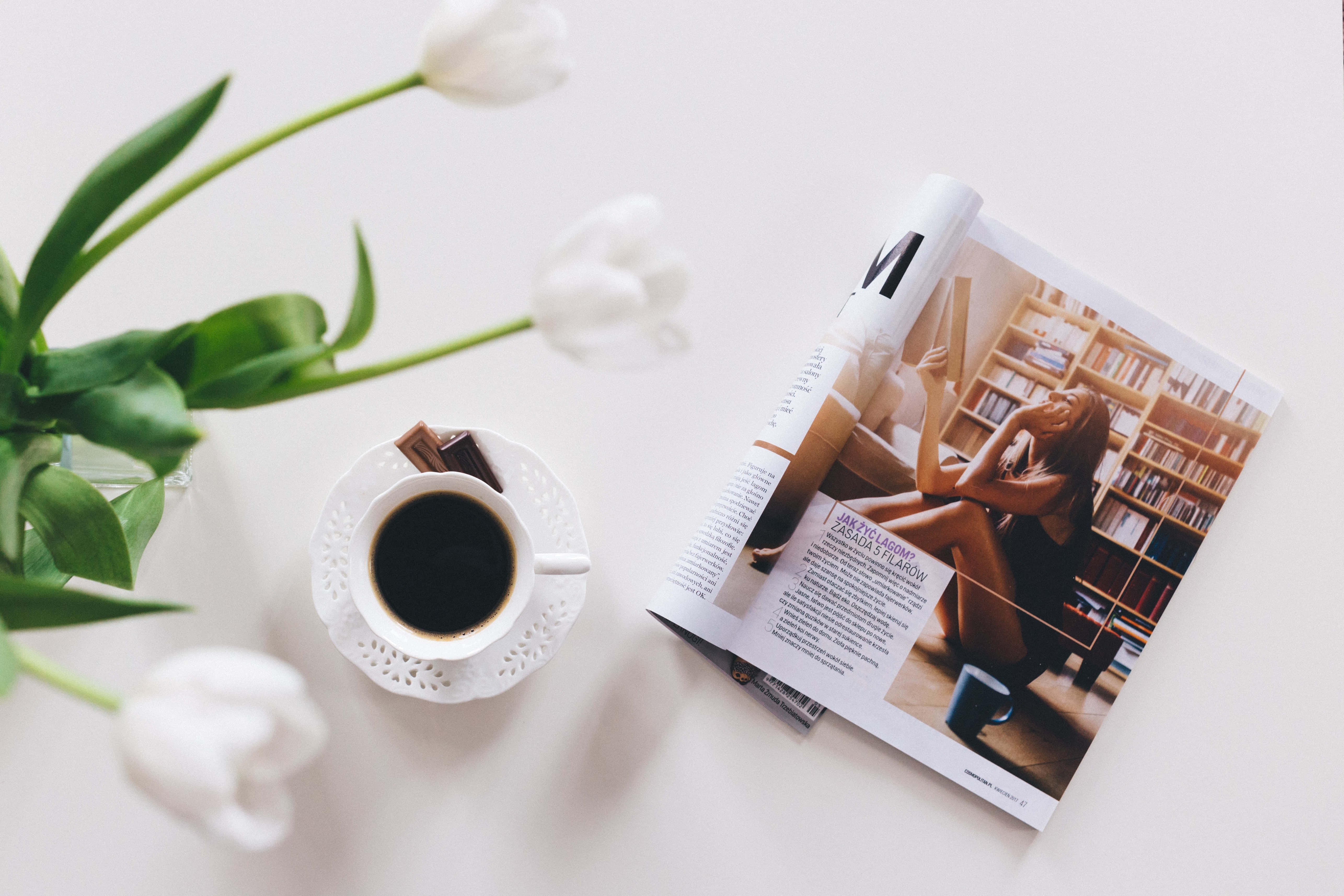 雜誌 桌布 壁紙 — 一個寧靜的平鋪構圖，包含白色鬱金香、一杯黑咖啡和一本打開的雜誌，置於潔白的表面上。