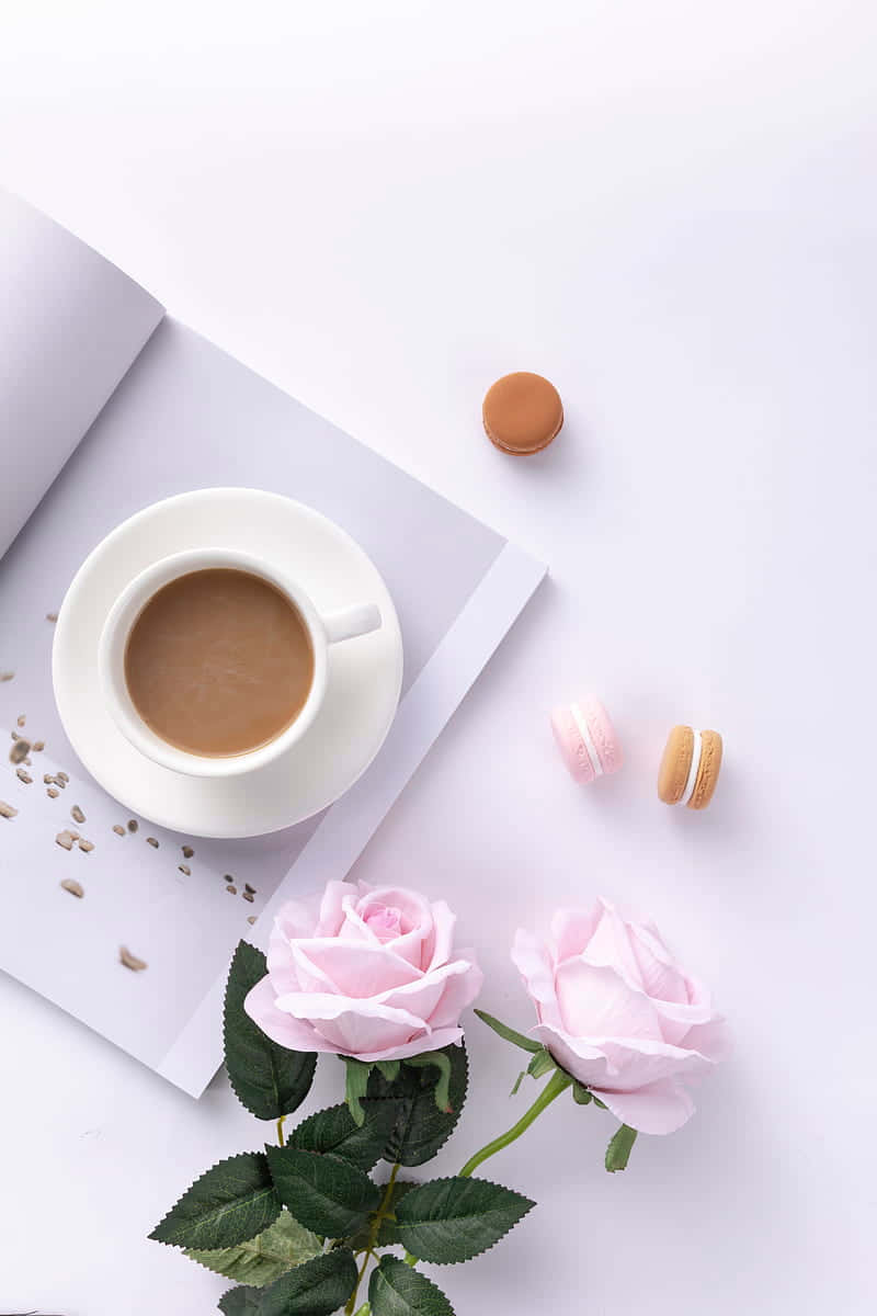 Coffee Aesthetic 桌布 壁紙 — 一個寧靜的平鋪構圖，包括一杯咖啡馬卡龍和粉紅玫瑰在白色表面上，散落著向日葵種子。