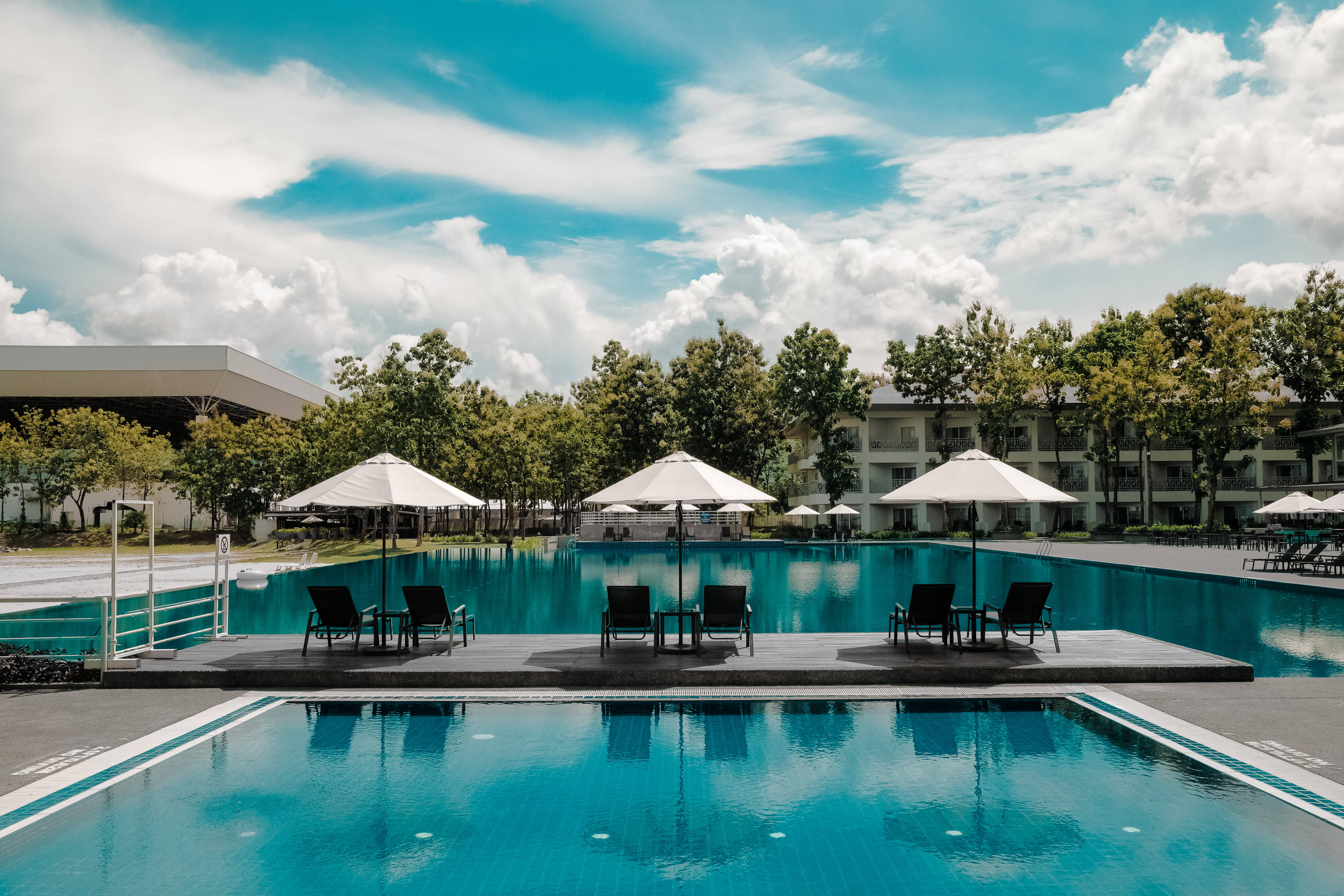 Hotel 桌布 壁紙 — 一個寧靜的度假村泳池，擁有碧綠色的水和白色遮陽傘，在明亮的藍天下有蓬鬆的雲朵。