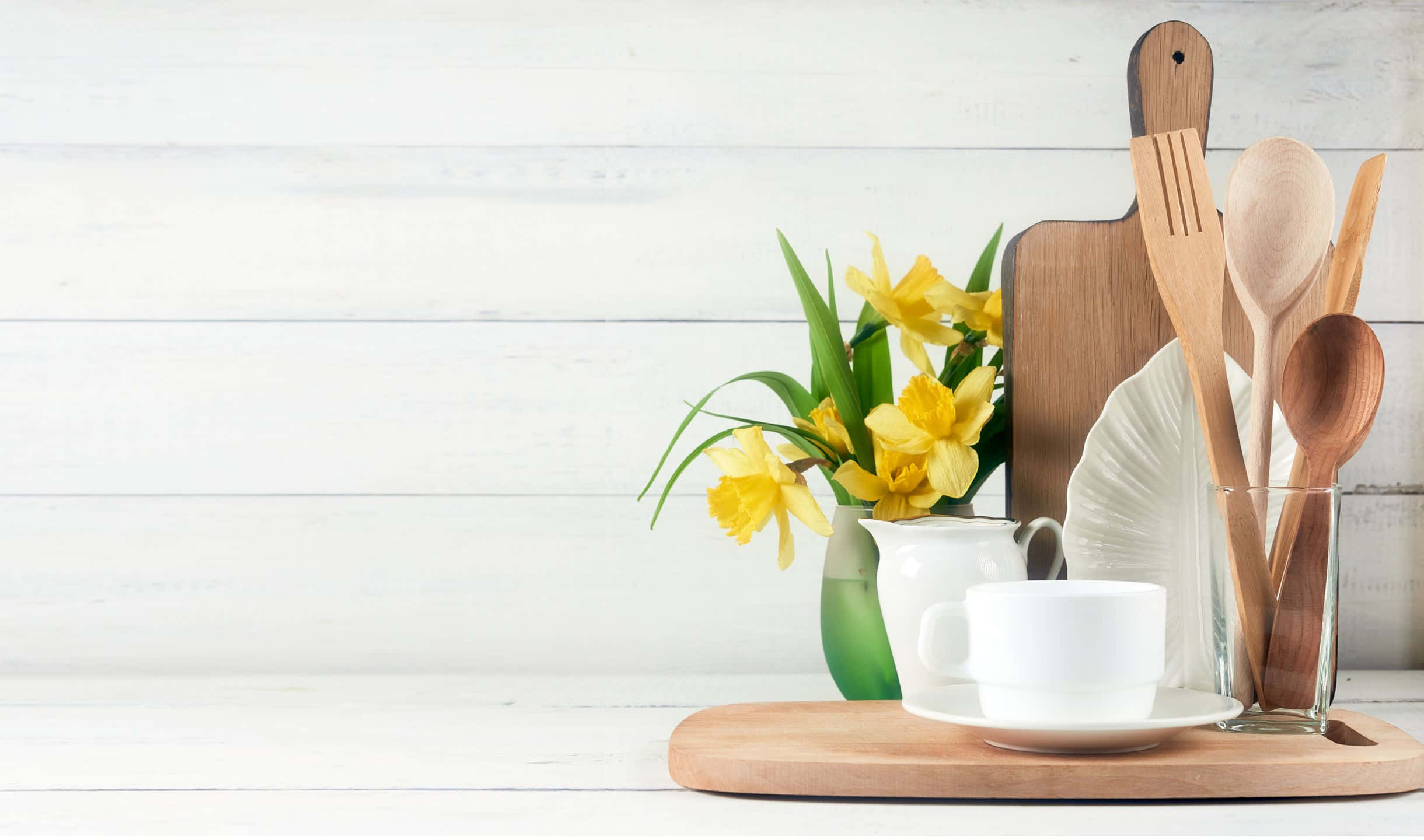 kitchen 桌布 壁紙 — 一個寧靜的廚房場景，綠色花瓶中的黃色水仙花旁邊放著白色咖啡杯和木製餐具，放在木托盤上，背景是白色木質背景。