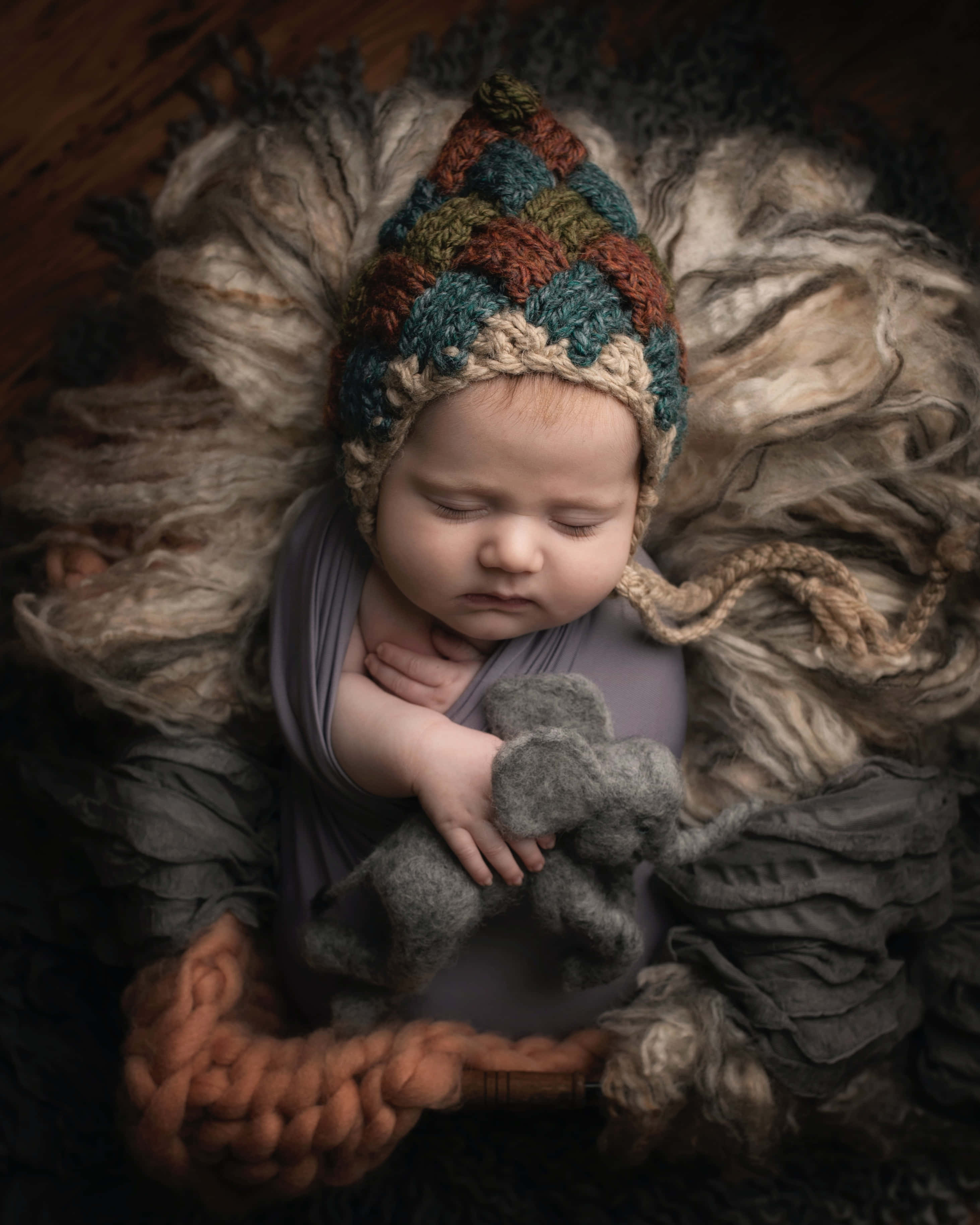 Baby Boy 桌布 壁紙 — 一個寧靜的新生兒在柔軟的質感中安詳入睡，戴著彩色針織帽，抱著一隻灰色氈毛大象。