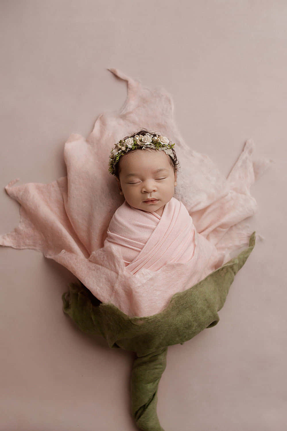 Newborn Baby 桌布 壁紙 — 一個寧靜的新生嬰兒包裹在柔軟的粉紅色布料中，安詳地躺在一朵大的綠色布料花內。