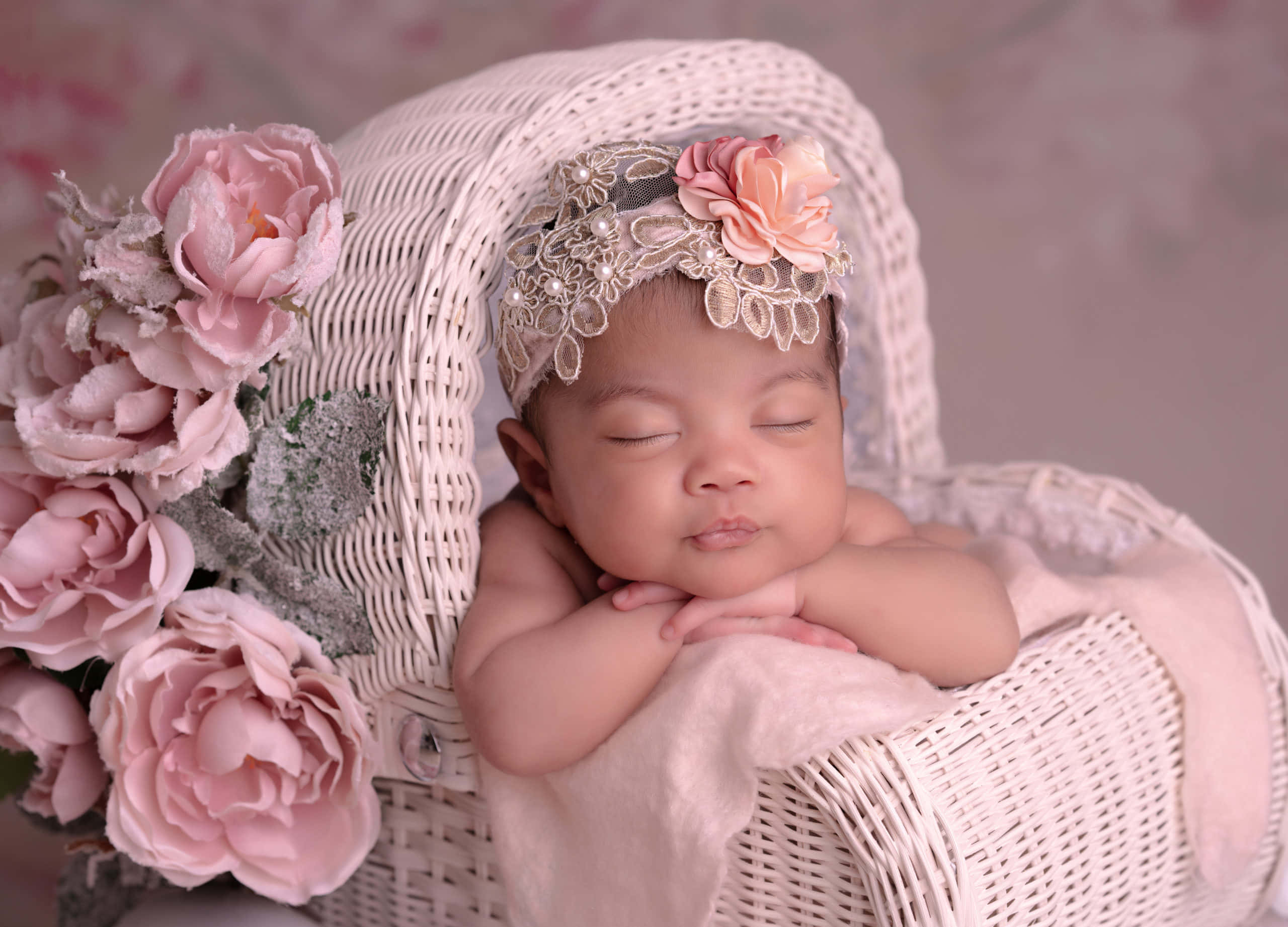 Newborn Baby 桌布 壁紙 — 一個寧靜的新生嬰兒在一個白色柳條籃中安詳地睡覺，籃子裝飾著柔和的粉紅玫瑰和一個花卉頭帶。