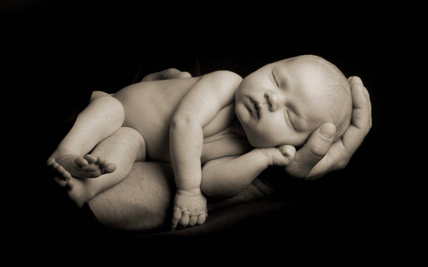 Newborn 桌布 壁紙 — 一個寧靜的新生嬰兒在成人手中安詳地睡著，背景是純黑色。