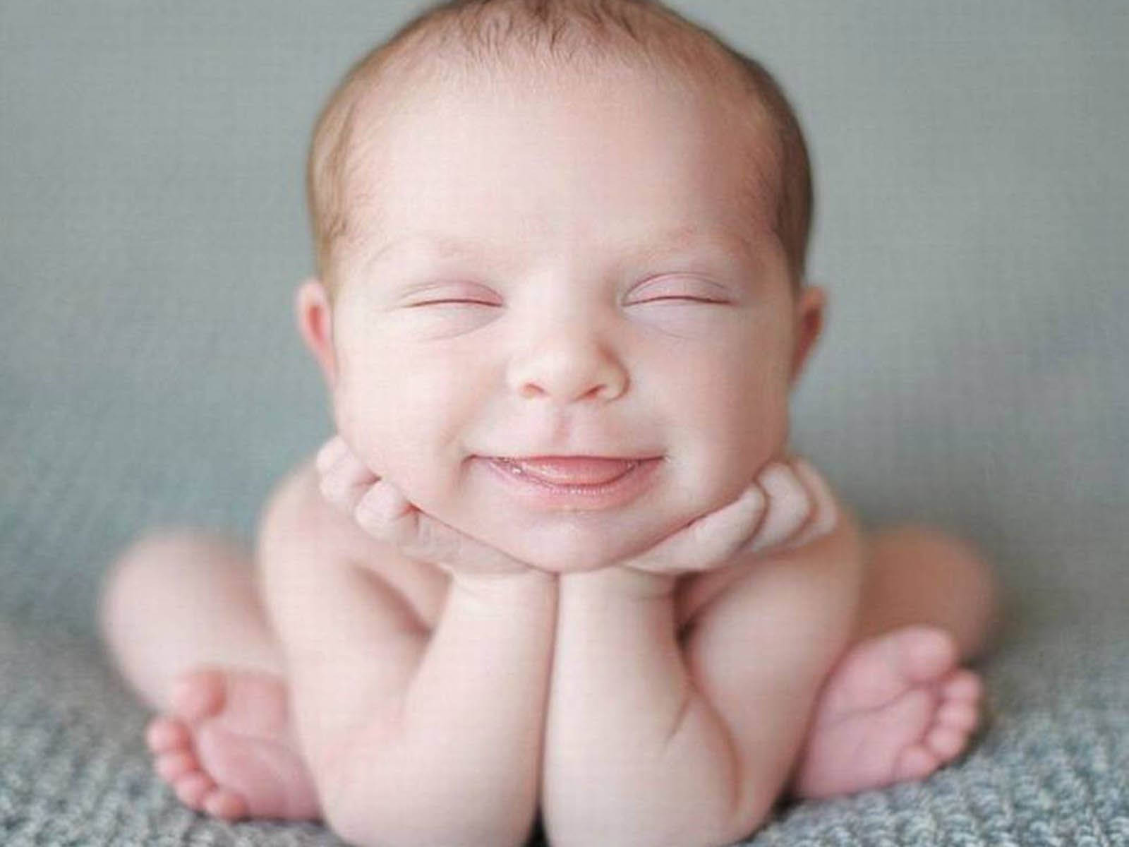 Funny Baby 桌布 壁紙 — 一個寧靜的新生嬰兒在柔軟有質感的毛毯上，下巴擱在小手上，帶著溫柔的微笑安詳地睡著。