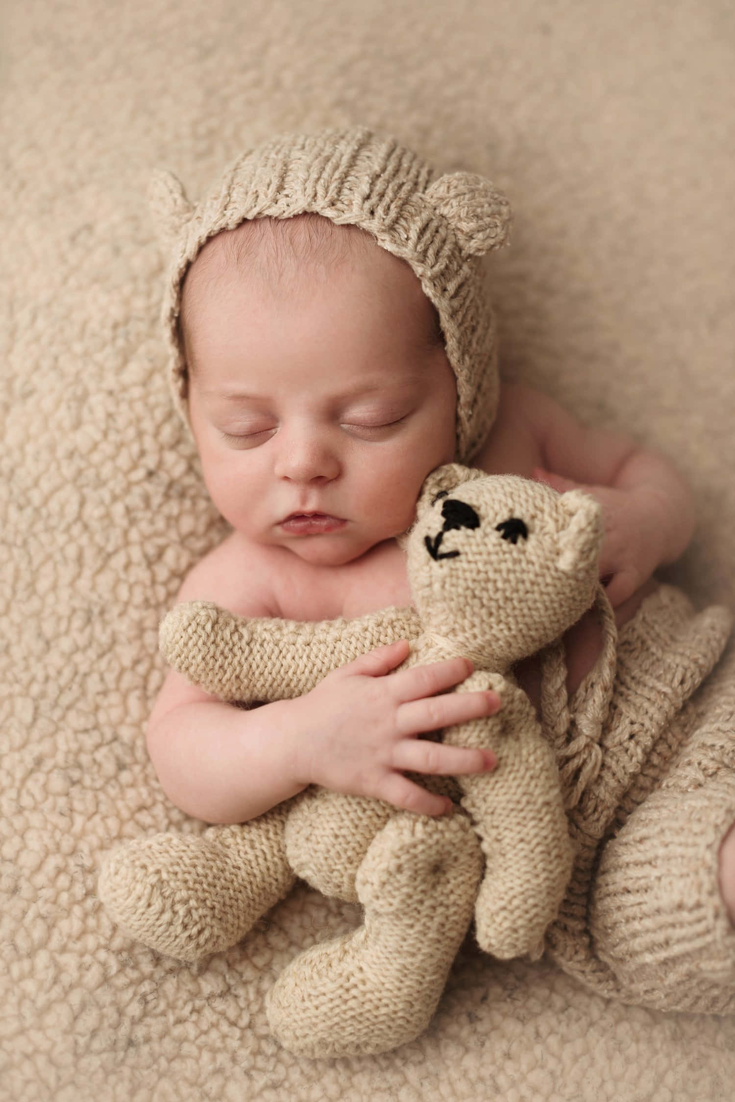 Newborn Baby 桌布 壁紙 — 一個寧靜的新生嬰兒在柔軟的米色紋理背景下，安詳地睡著，緊握著一隻針織泰迪熊。