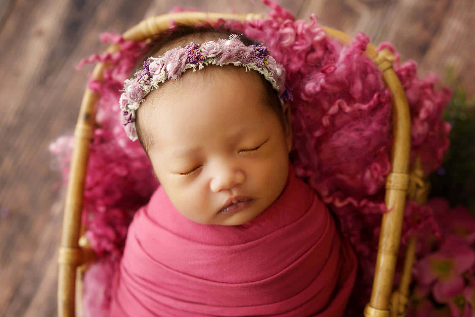 Newborn Baby 桌布 壁紙 — 一個寧靜的新生嬰兒被粉紅色布料包裹著，安詳地睡在一個內襯蓬鬆洋紅色材料的柳條籃子裡。