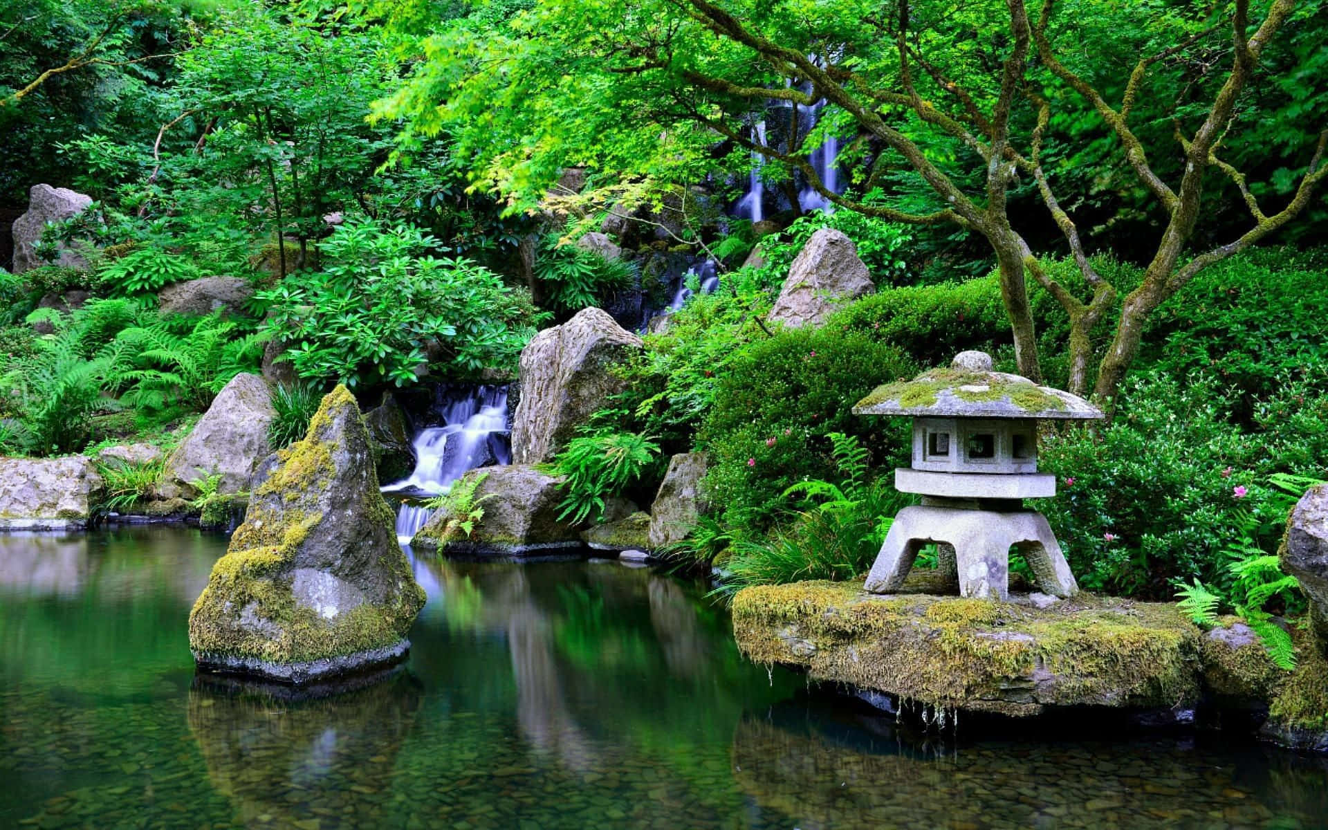 Enchanted Garden 桌布 壁紙 — 一個寧靜的日本花園池塘，有長滿苔蘚的岩石、瀑布和一個石燈籠，周圍環繞著茂密的綠色樹葉。