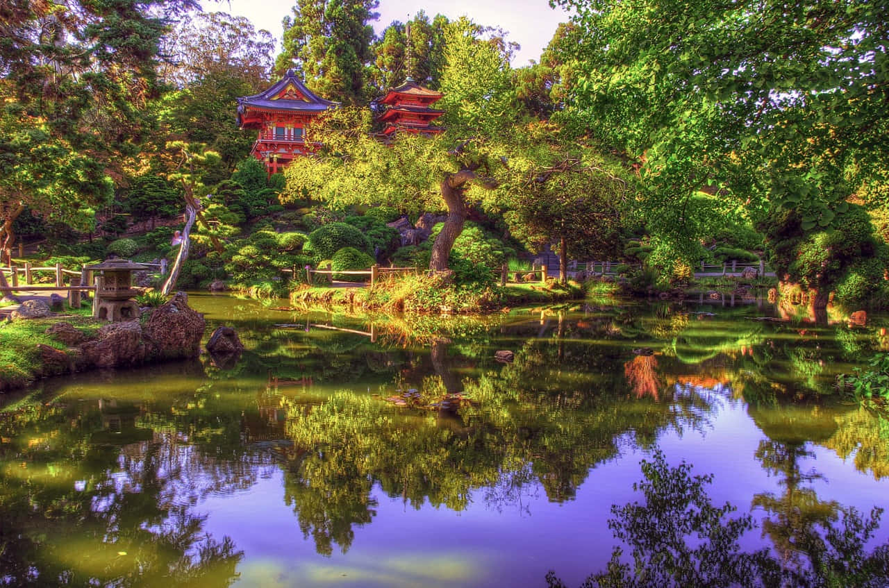 Samurai Garden 桌布 壁紙 — 一個寧靜的日本花園池塘在明亮的日光下倒映著充滿活力的綠樹和傳統的紅色寶塔。