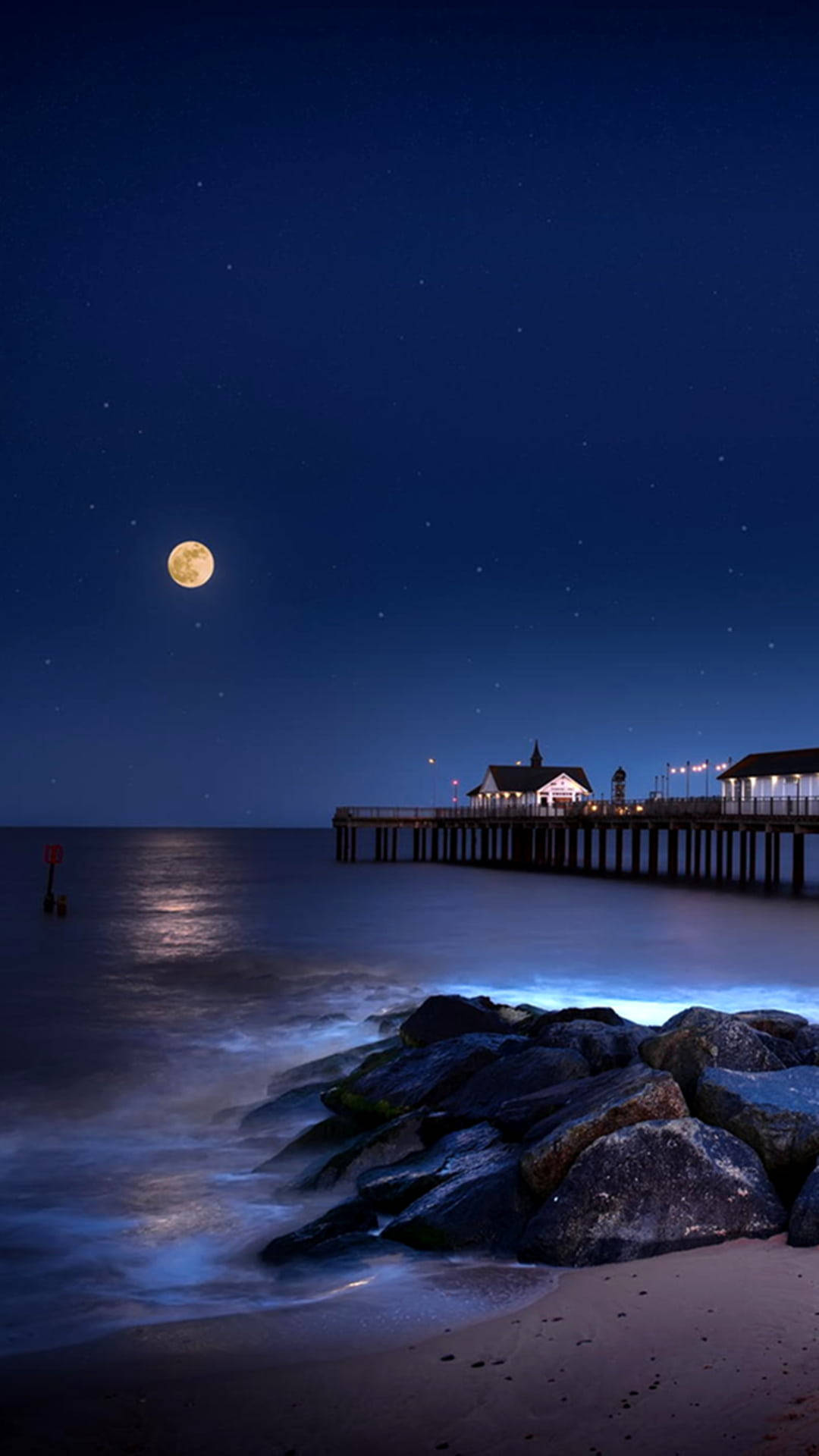 Beach Scene 桌布 壁紙 — 一個寧靜的月夜海灘，星空閃爍，月亮發光，碼頭延伸至平靜的水面。