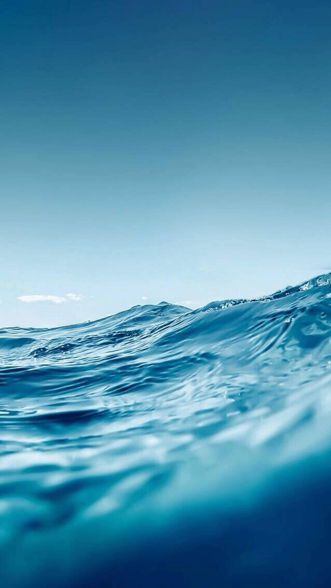 Ocean iPhone 桌布 壁紙 — 一個寧靜的水底視角，透過漣漪的藍色海浪向上望向有遠處雲朵的清澈天空。
