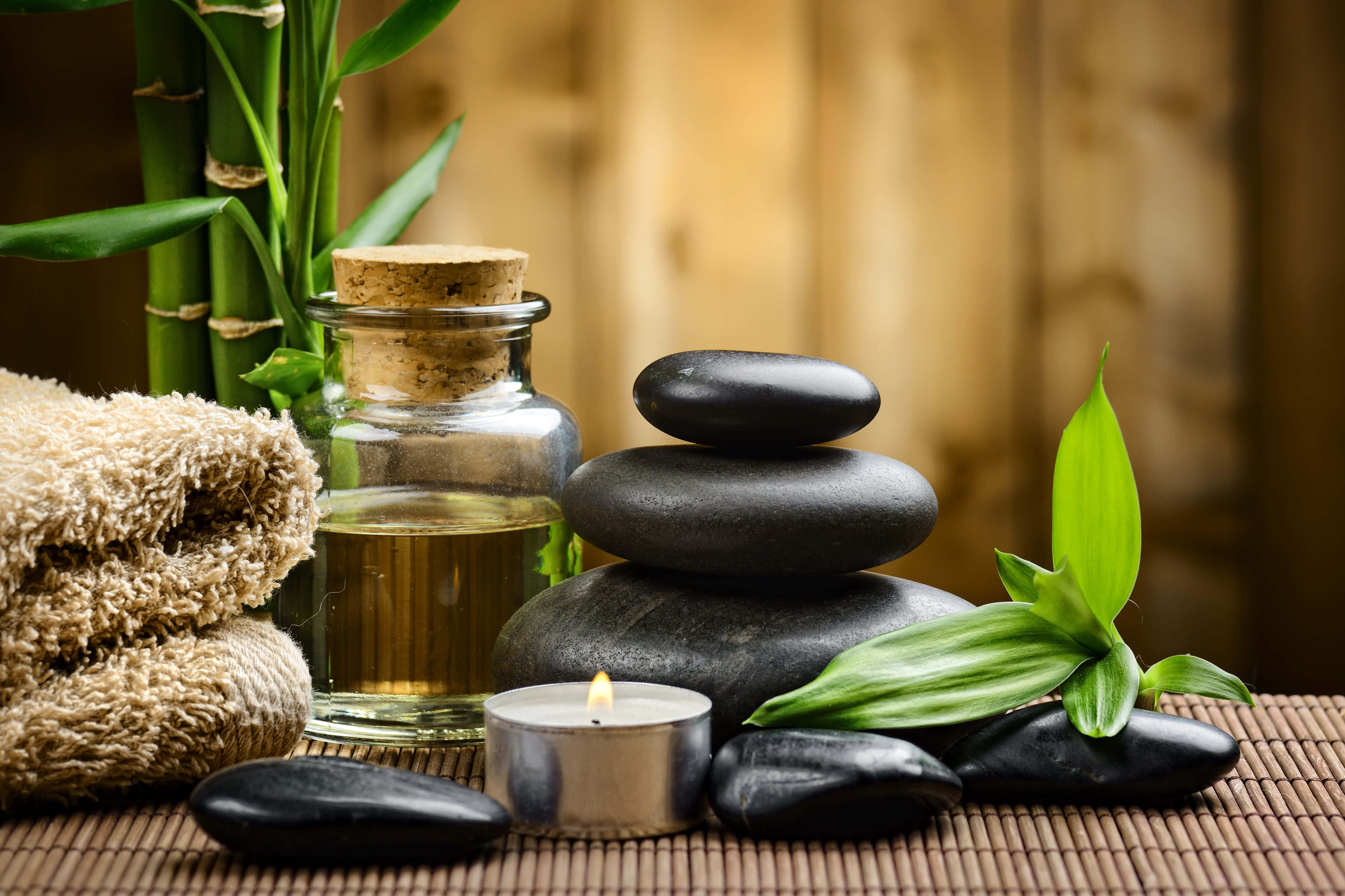 Spa Treatments 桌布 壁紙 — 一個寧靜的水療佈置，包含疊放的黑石、點燃的蠟燭、竹葉和一個玻璃瓶的油放在編織墊上。