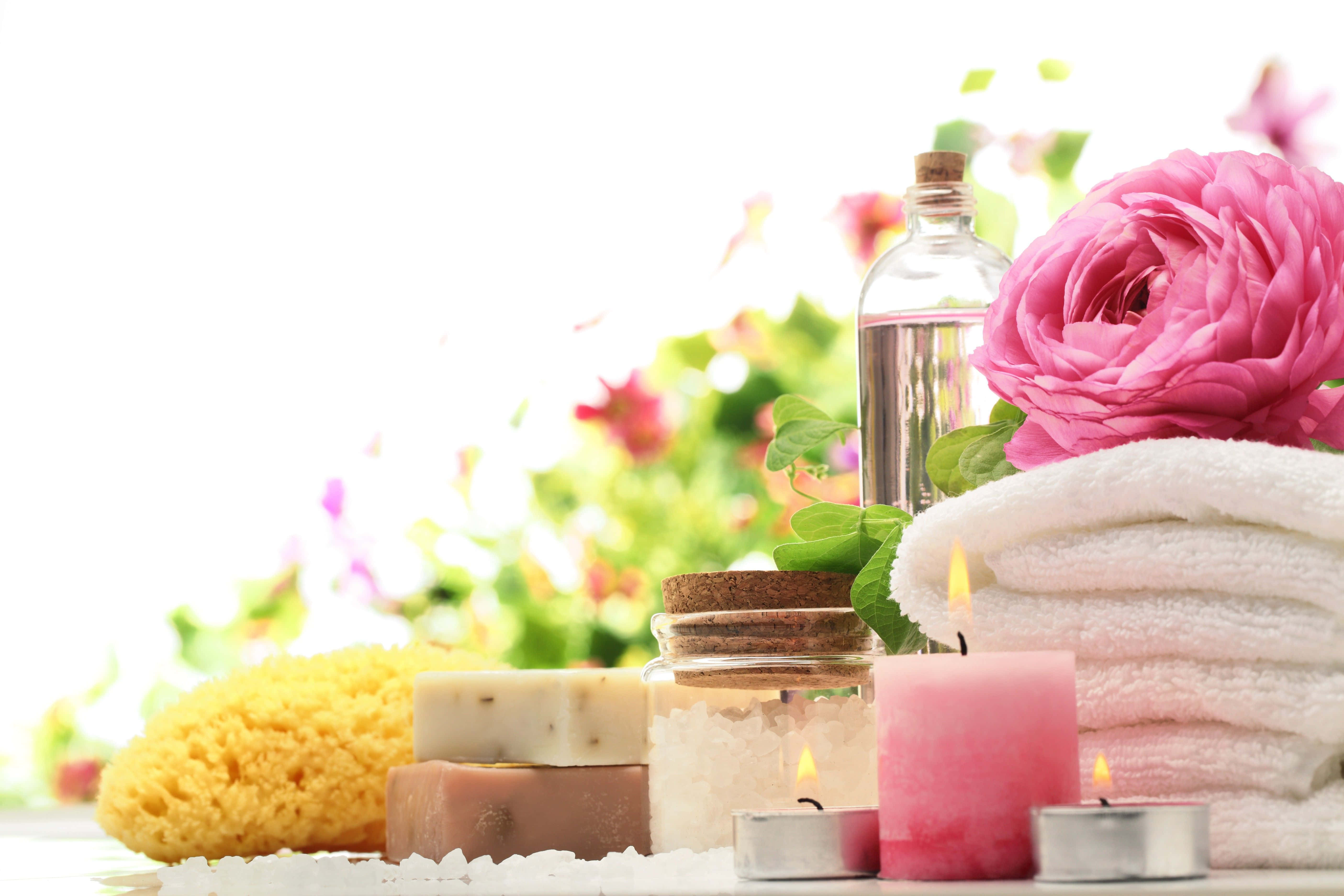 Health And Beauty 桌布 壁紙 — 一個寧靜的水療佈置，配有粉紅玫瑰、點燃的蠟燭和沐浴必需品，背景是明亮的花卉圖案。