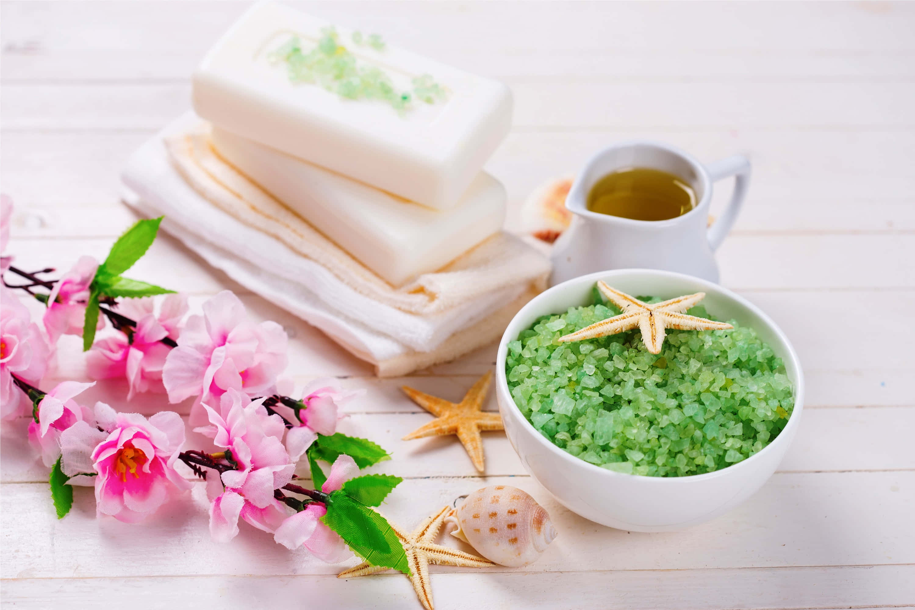Spa Treatments 桌布 壁紙 — 一個寧靜的水療設置，包含綠色鹽、海星、粉紅櫻花和堆疊的肥皂在白色木質表面上。