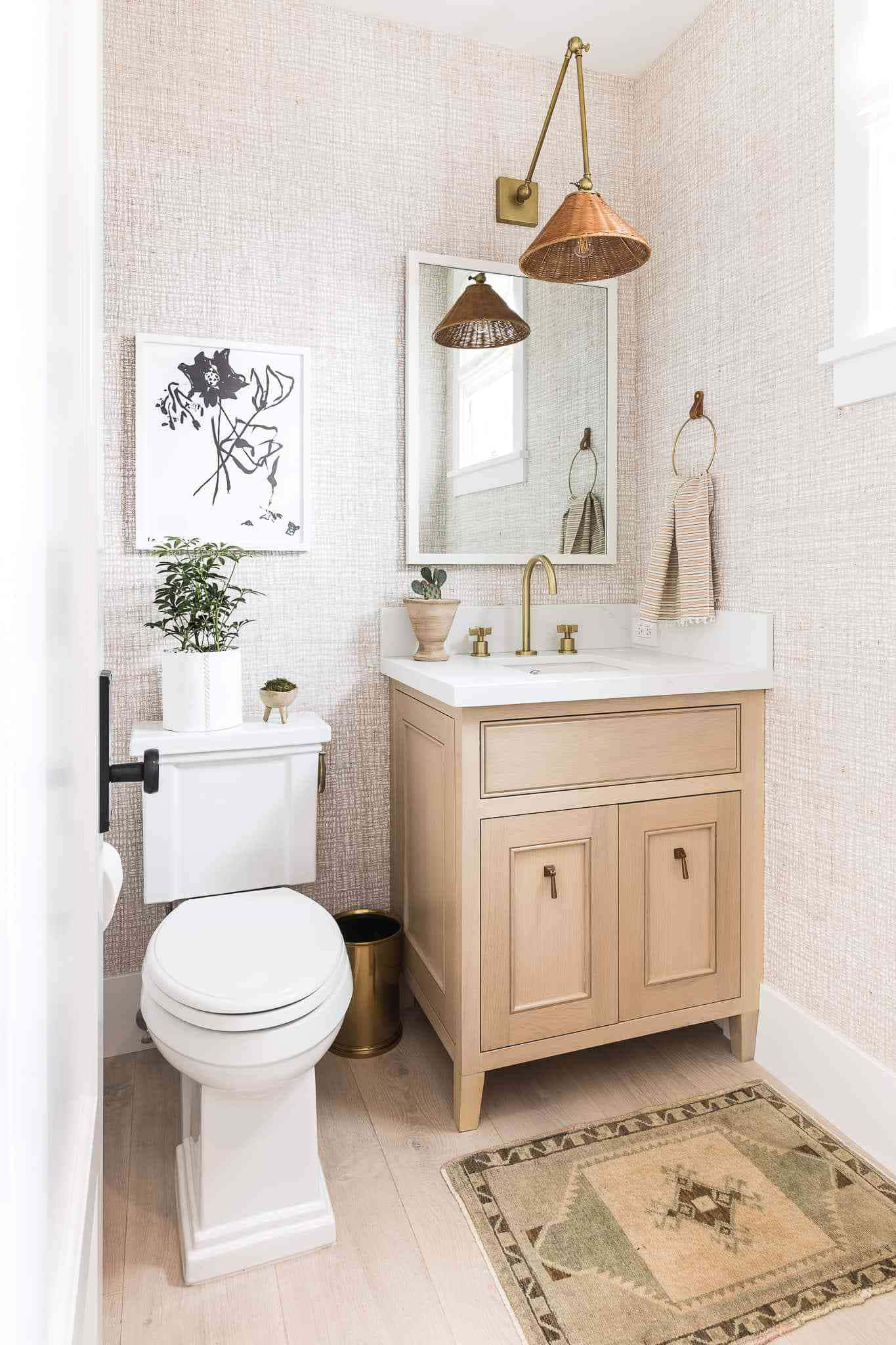 Bathroom Decor 桌布 壁紙 — 一個寧靜的浴室，配有淺色木製洗手台、黃銅配件和紋理粉紅色牆壁，並有復古地毯和黑白藝術品。