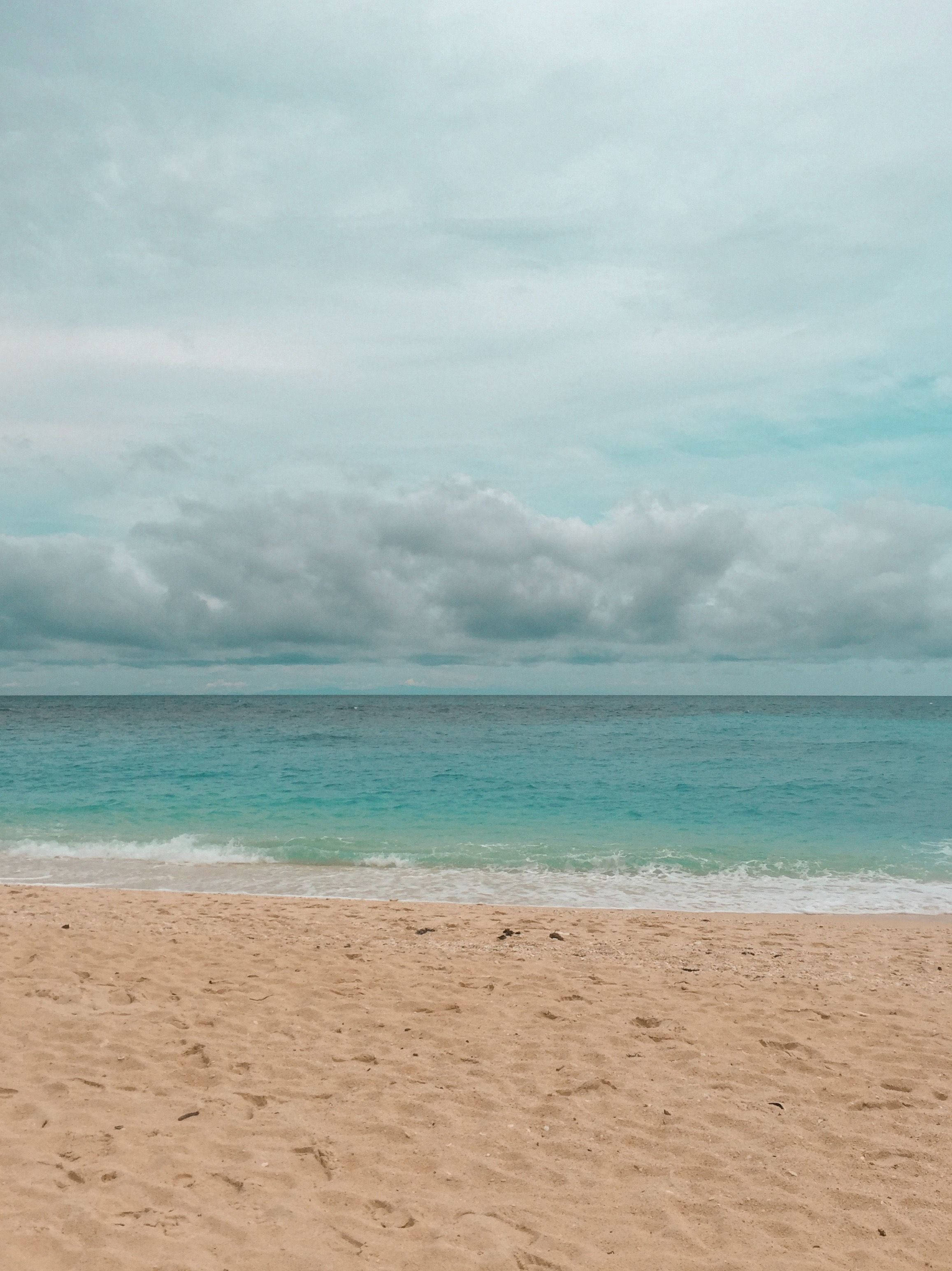 海洋 桌布 壁紙 — 一個寧靜的海灘場景，在陰天之下，碧綠色的海浪輕拍著金色的沙灘。