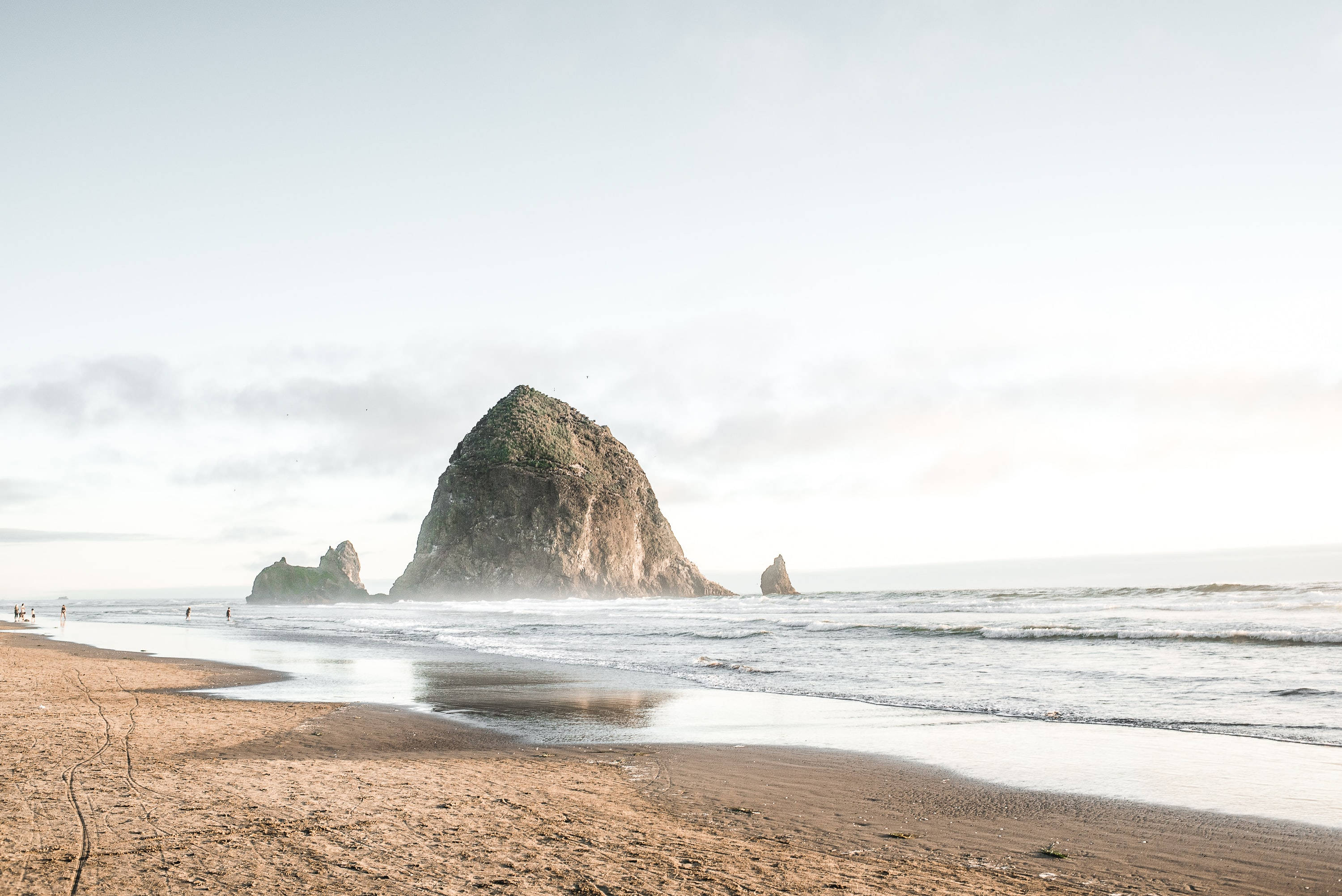 Oregon 桌布 壁紙 — 一個寧靜的海灘場景，巨大的長滿苔蘚的岩石從海洋中升起，天空柔和多雲。