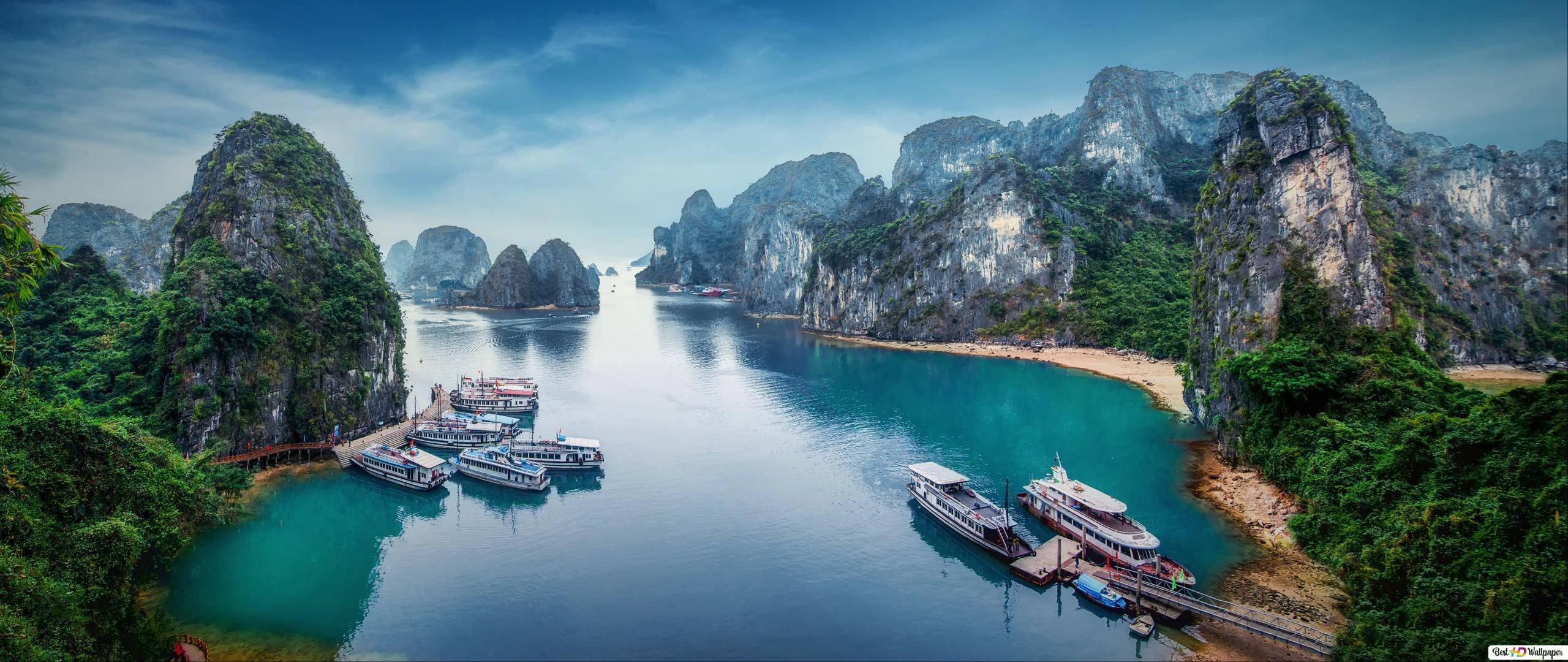 Asia 桌布 壁紙 — 一個寧靜的海灣，擁有碧綠的海水，周圍環繞著高聳的石灰岩喀斯特地貌，覆蓋著茂密的綠色植物，並點綴著停泊的船隻。
