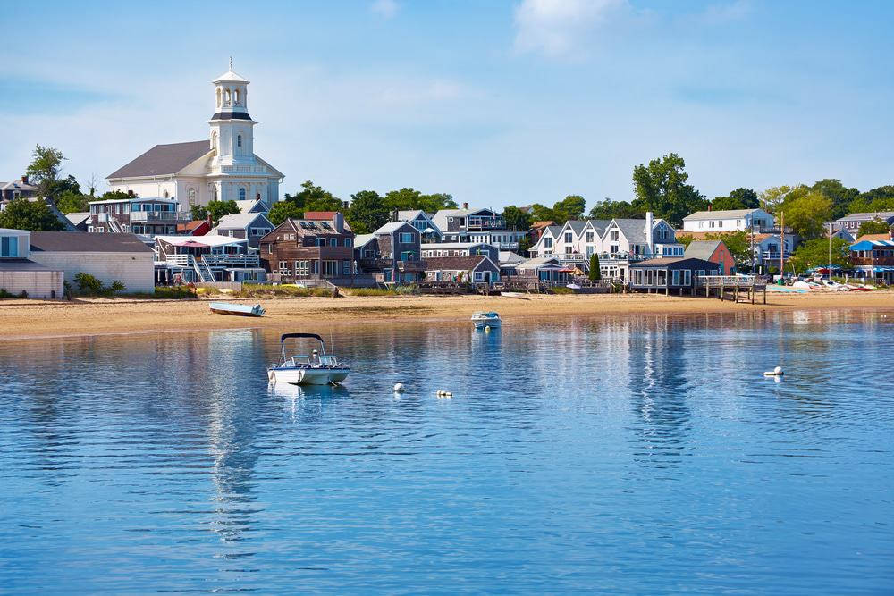 Massachusetts 桌布 壁紙 — 一個寧靜的海邊小鎮，色彩繽紛的房屋和白色教堂倒映在平靜的藍色海水中，天空晴朗。