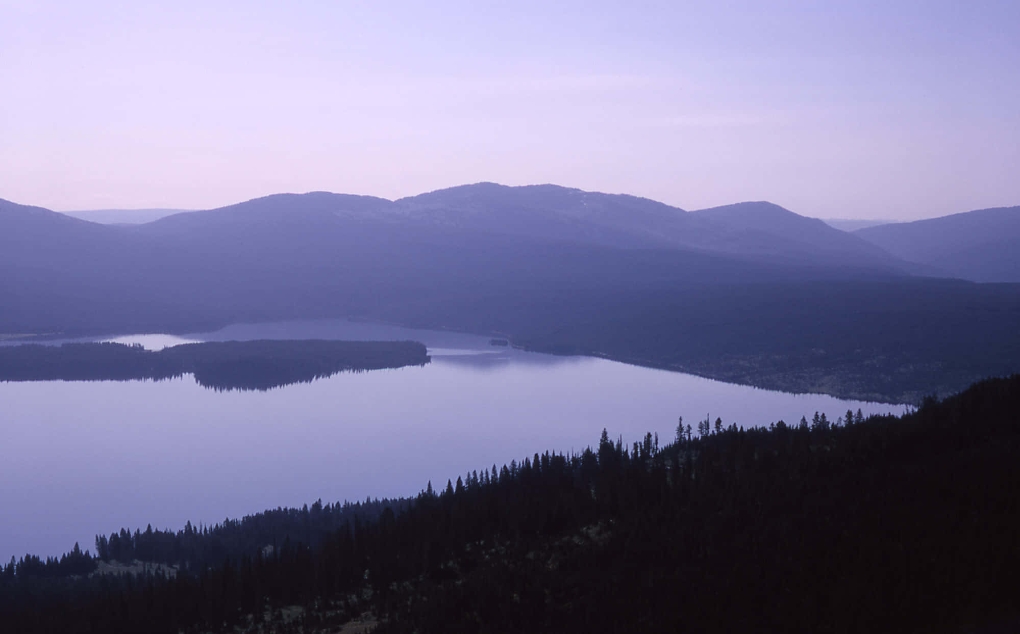 Yellowstone 桌布 壁紙 — 一個寧靜的湖泊，坐落在遙遠的山巒之間，在柔和的紫色暮色天空下。