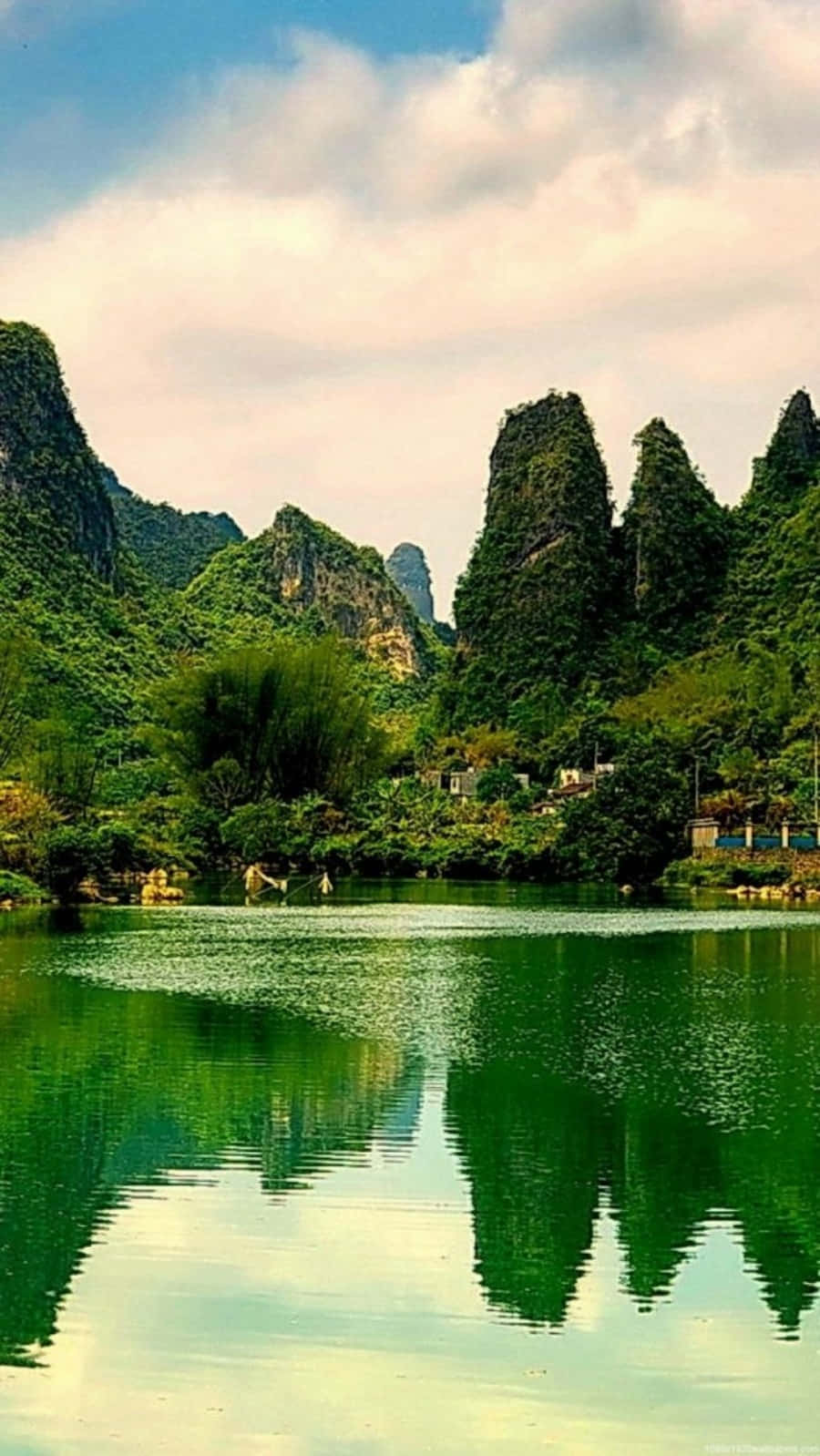 美麗風景動圖 桌布 壁紙 — 一個寧靜的湖泊在部分多雲的天空下，映照出鬱鬱蔥蔥的綠色喀斯特山脈，帶有鮮豔的倒影。