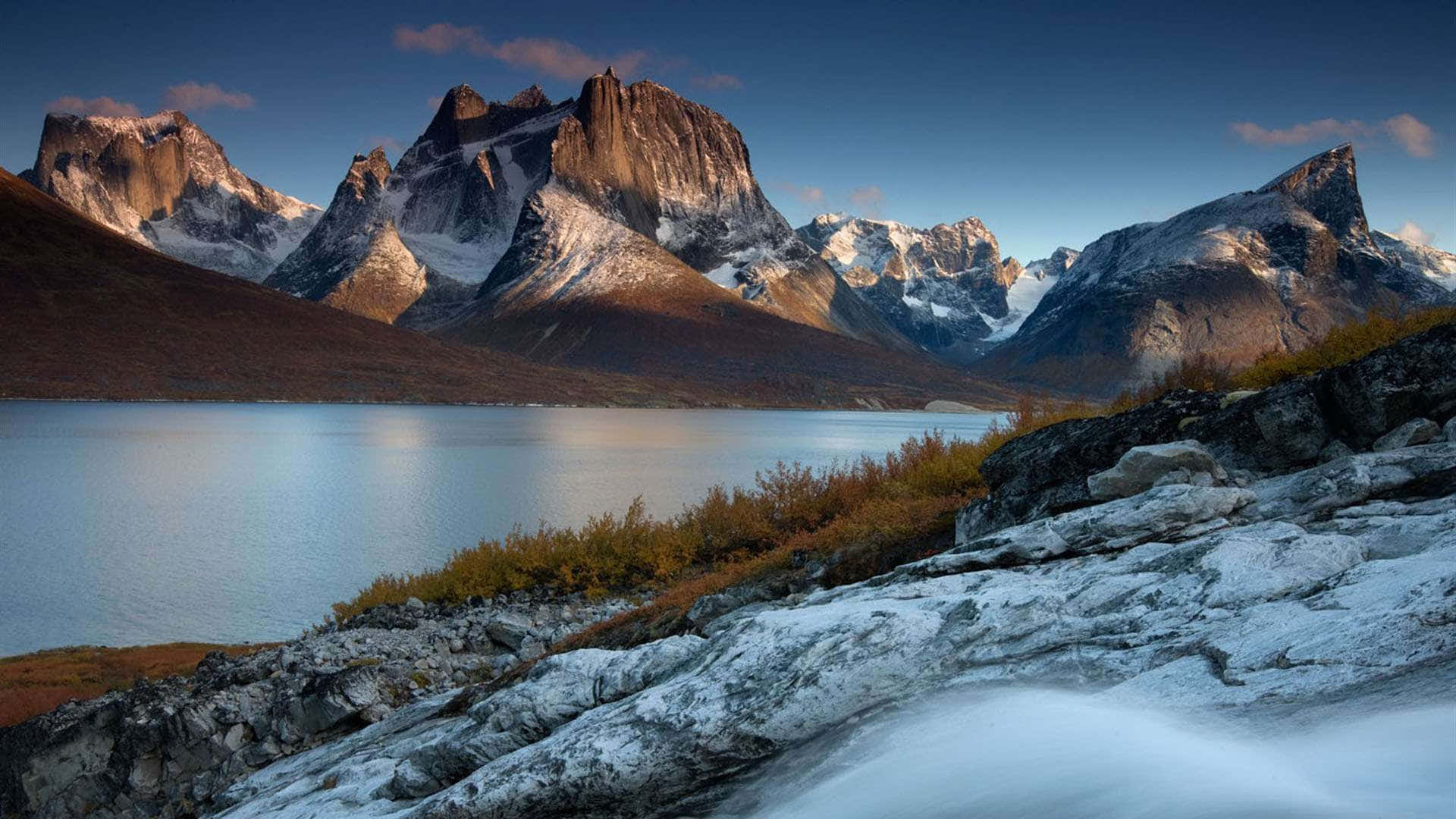 Greenland 桌布 壁紙 — 一個寧靜的湖泊映照著白雪覆蓋的山脈，在暮色天空下，崎嶇的山峰上閃耀著金色的光芒。