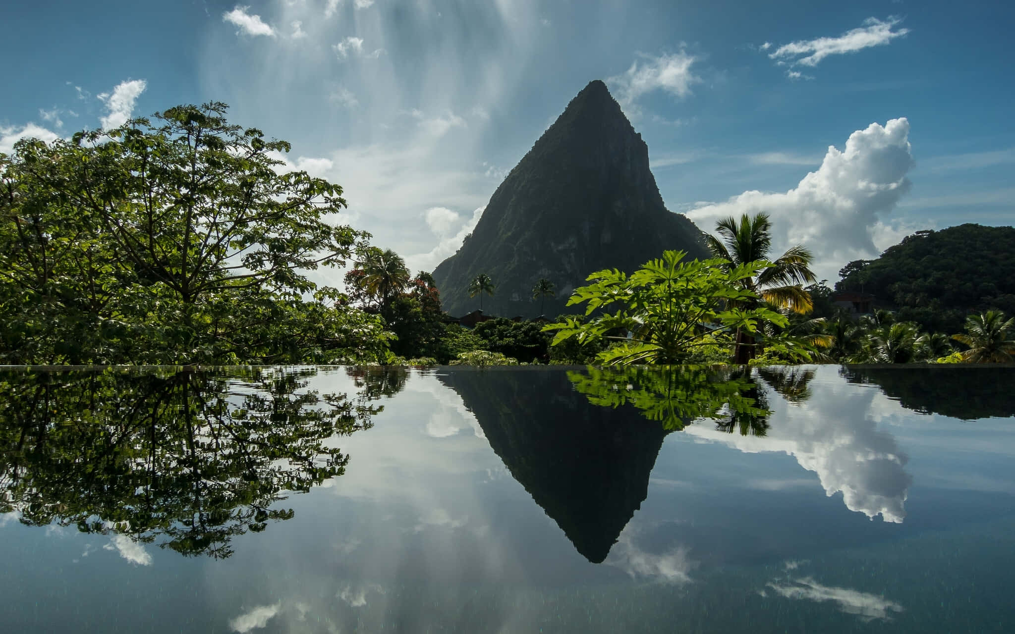 Caribbean 桌布 壁紙 — 一個寧靜的無邊際泳池映照著高聳的皮通山和茂密的綠植，天空湛藍，白雲點綴。