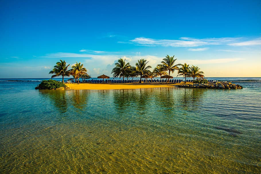 Jamaica 桌布 壁紙 — 一個寧靜的熱帶島嶼，棕櫚樹和躺椅坐落在清澈碧綠的海水中，上方是充滿活力的藍天。