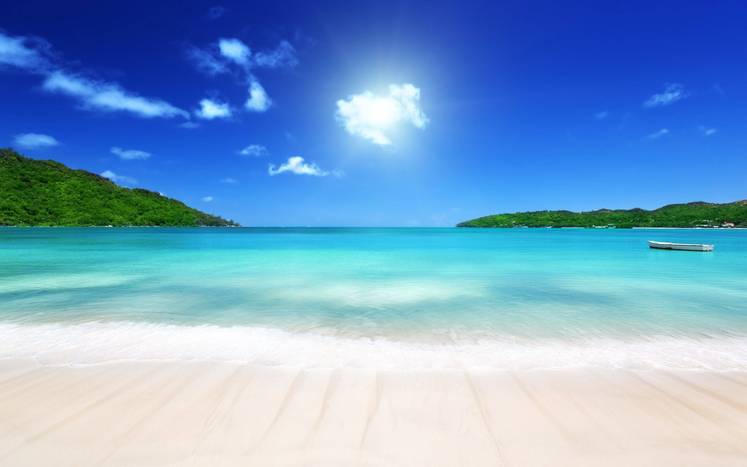 Tropical 桌布 壁紙 — 一個寧靜的熱帶海灘，擁有碧綠的海水、溫柔的海浪和鬱鬱蔥蔥的綠色山丘，在明亮的藍天和蓬鬆的白雲下。