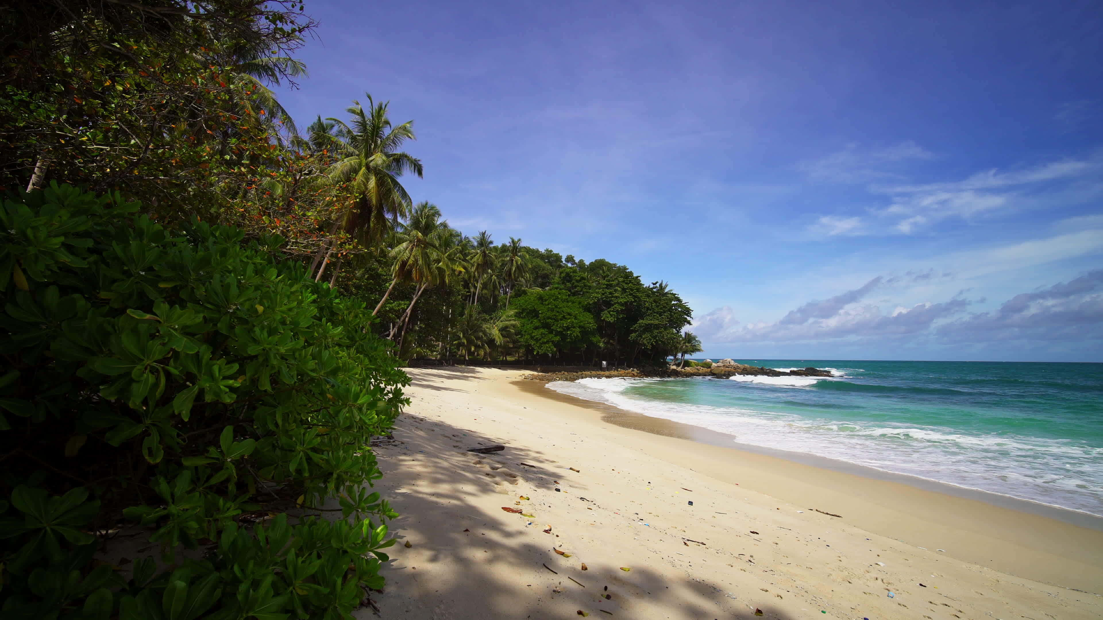 Beautiful Beach 桌布 壁紙 — 一個寧靜的熱帶海灘，白色沙灘在清澈藍天下沿著碧綠海浪輕輕彎曲。
