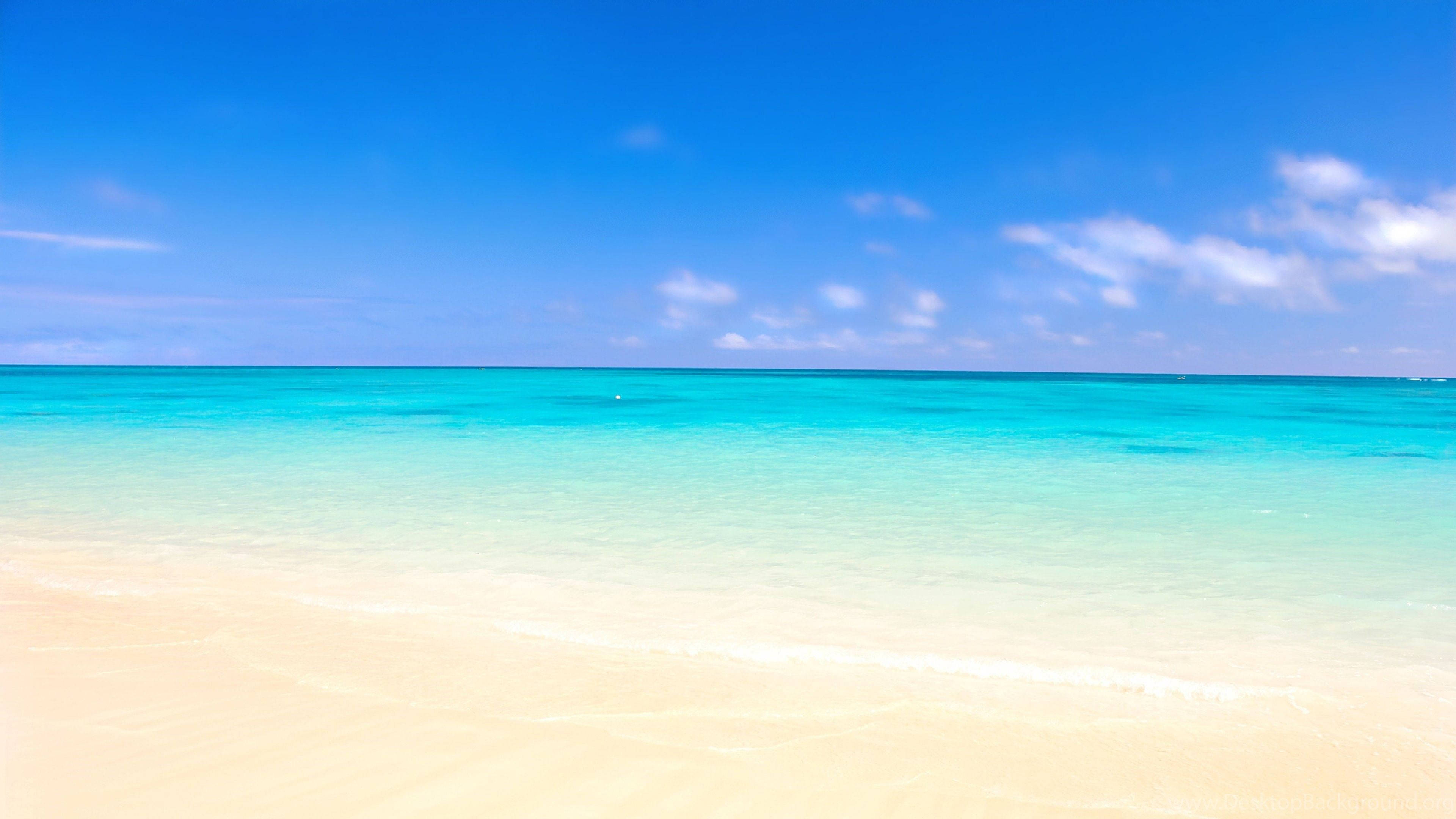 Beach Scenes Desktop 桌布 壁紙 — 一個寧靜的熱帶海灘，碧綠的海水輕輕拍打柔軟的白沙，頭頂是清澈的藍天。