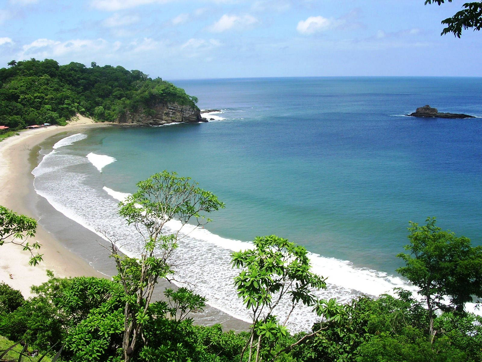 Nicaragua 桌布 壁紙 — 一個寧靜的熱帶海灣，擁有碧綠的海水、溫柔的海浪、沙灘和茂密的綠色叢林，在明亮的藍天下勾勒出海岸線。