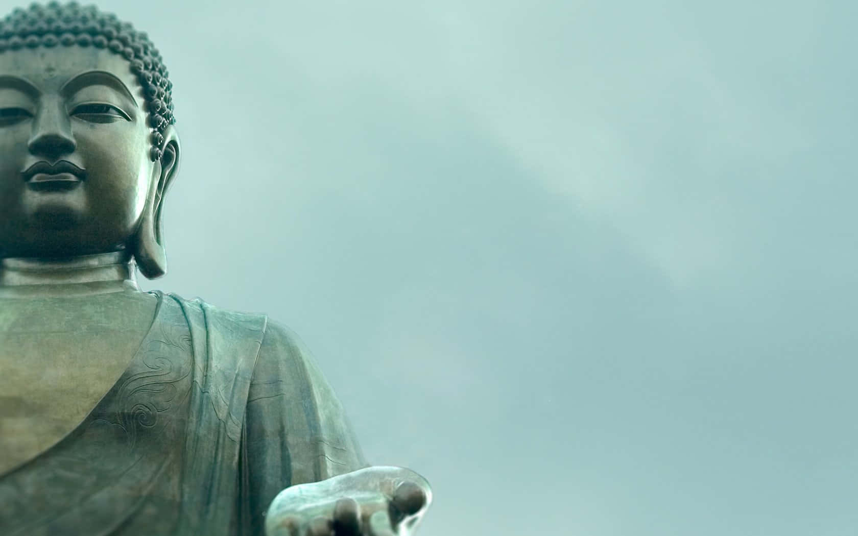 佛陀 桌布 壁紙 — 一個寧靜的特寫鏡頭，展示一尊大型青銅佛像，眼神平靜，手伸出，背景是柔和朦朧的天空。