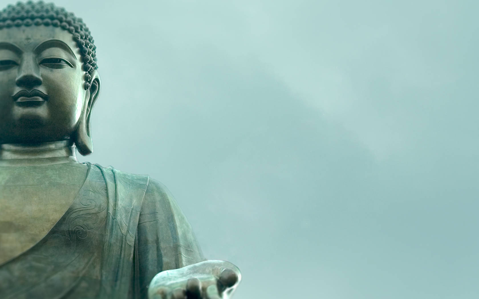 佛陀 桌布 壁紙 — 一個寧靜的特寫鏡頭，展示一尊大型青銅佛像，眼神平靜，手伸出，背景是柔和的青綠色天空。