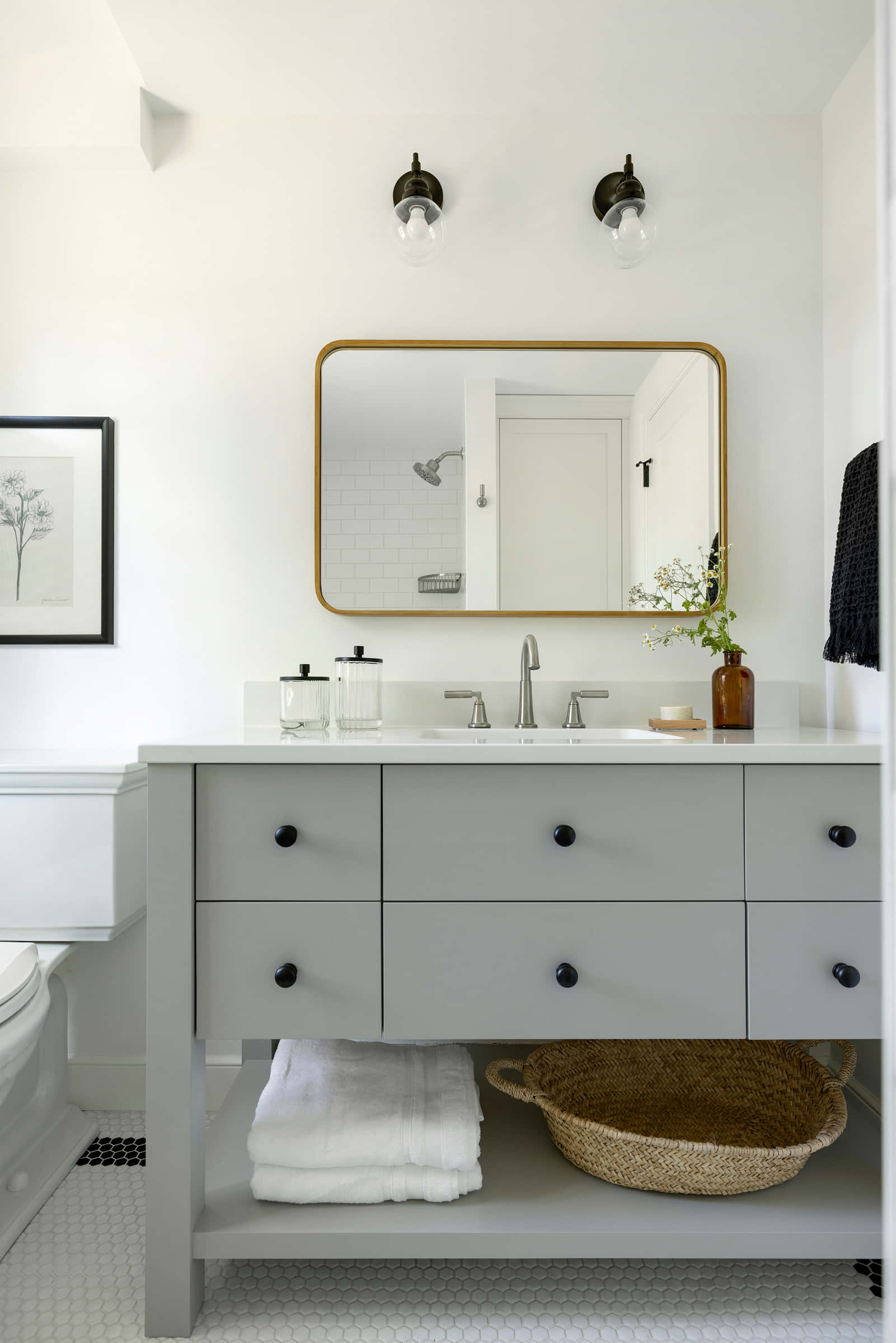 Black And White Bathroom 桌布 壁紙 — 一個寧靜的現代浴室，配有灰色梳妝台、白色六角形瓷磚地板和金色鏡框的鏡子，反射出潔淨的白色淋浴間。