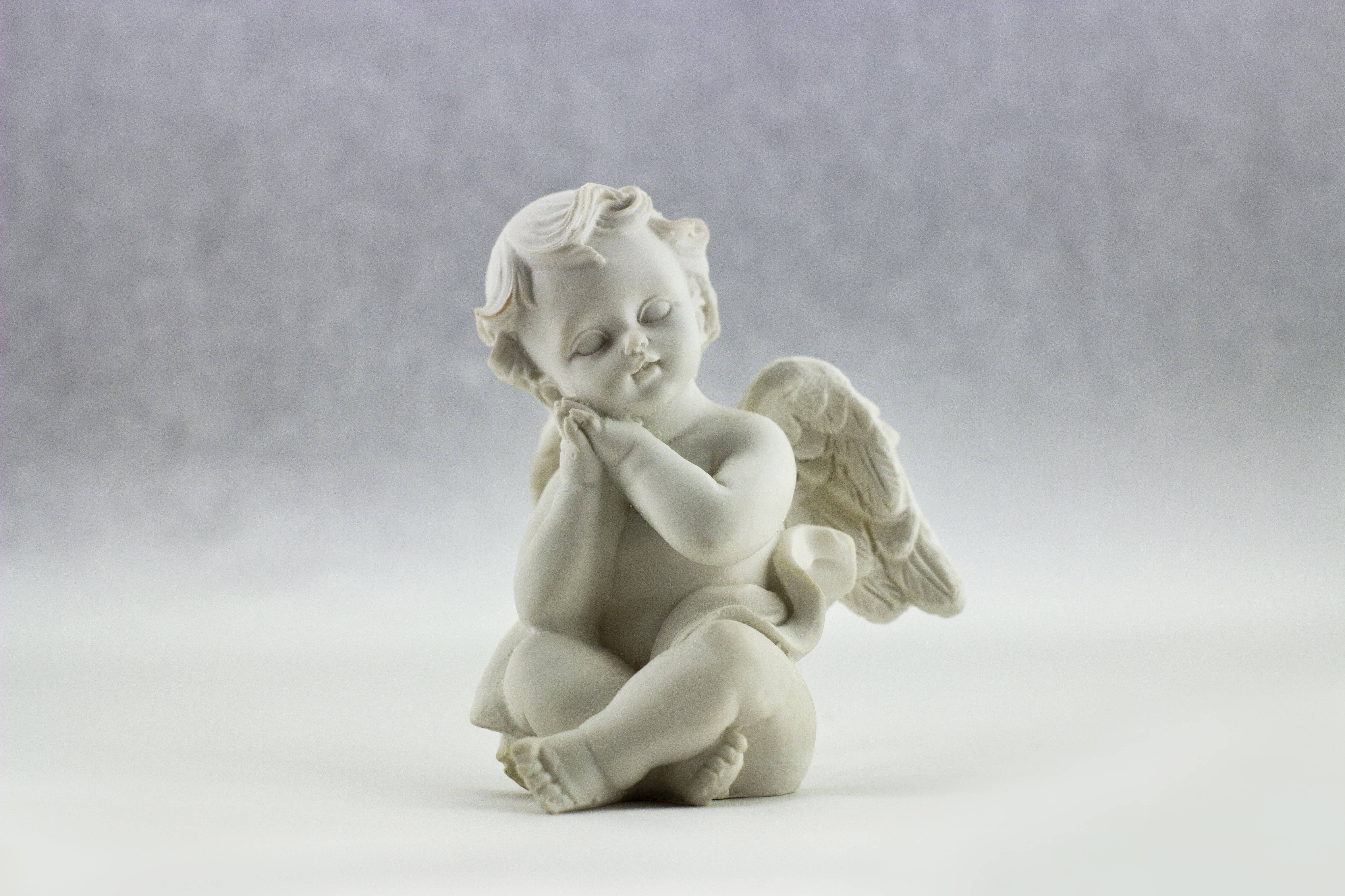 angels 桌布 壁紙 — 一個寧靜的白色大理石小天使雕像，閉著眼睛，帶著精緻的翅膀，坐在柔和的灰色背景前祈禱。