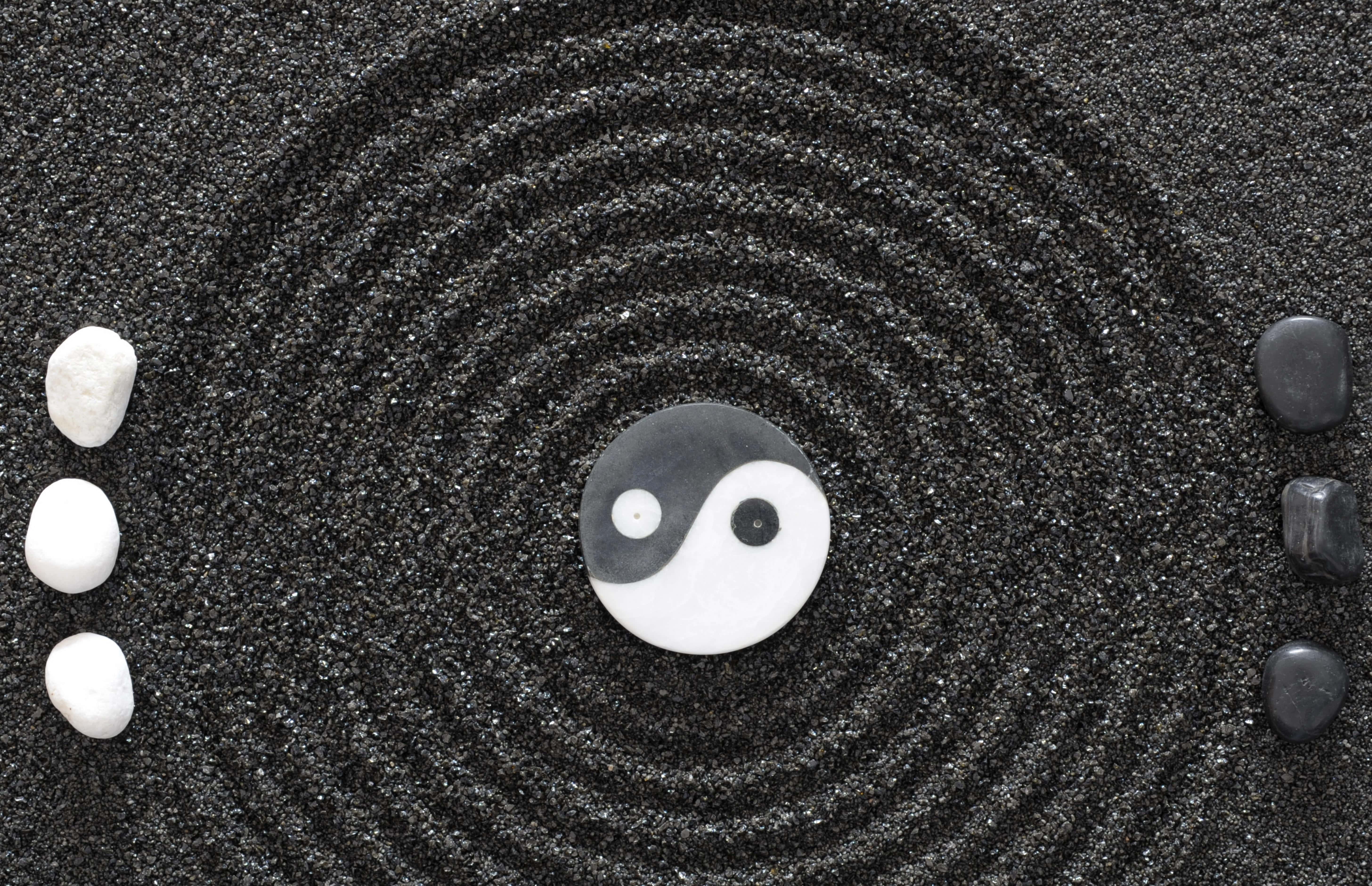 Yin Yang 4K 桌布 壁紙 — 一個寧靜的禪意花園，中央有陰陽石，周圍是同心圓的黑色沙紋和對比鮮明的白色與黑色石頭。