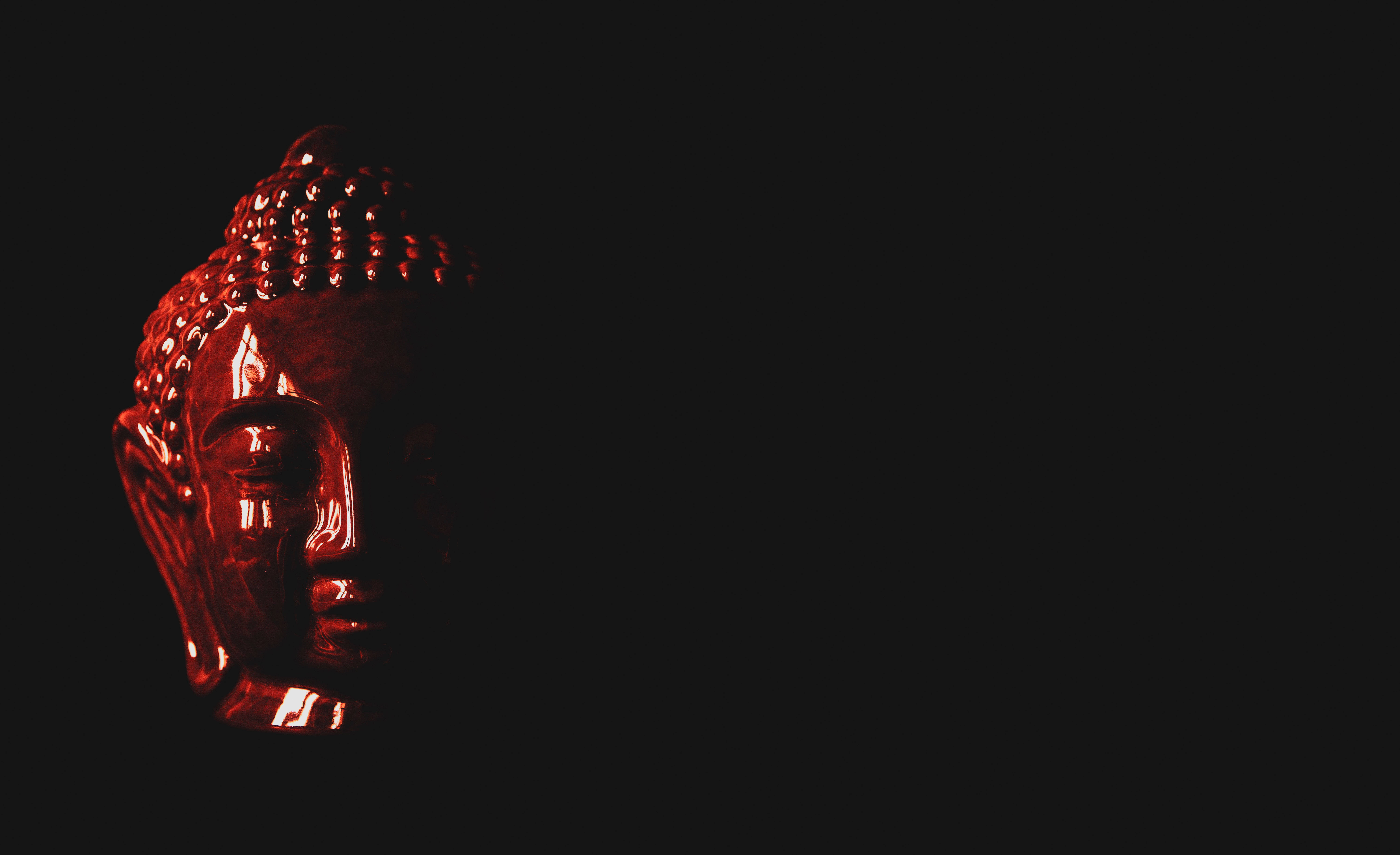 black buddha 桌布 壁紙 — 一個寧靜的紅色佛像頭雕塑在漆黑背景下以戲劇性燈光發光。