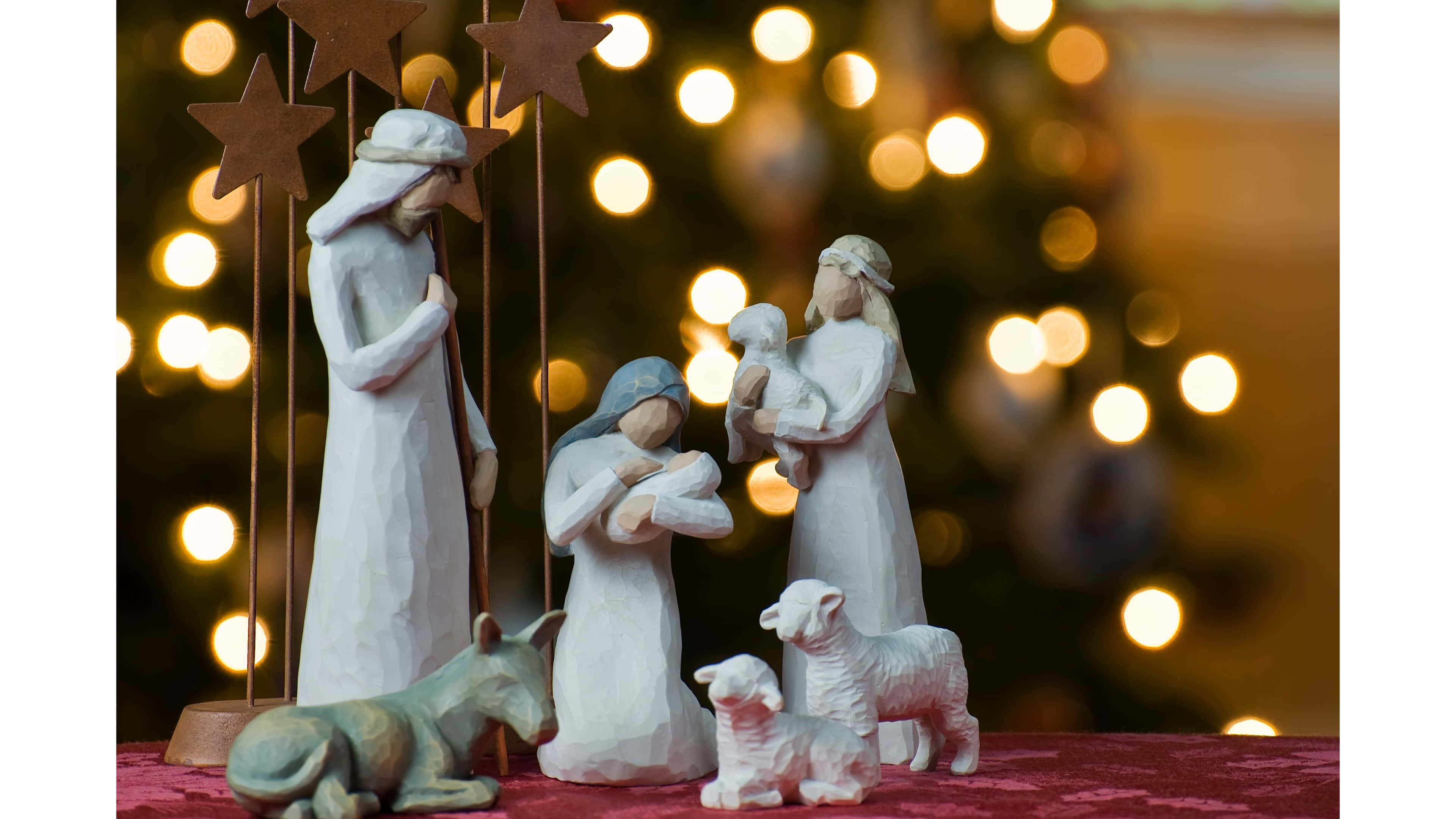 Religious Christmas 桌布 壁紙 — 一個寧靜的耶穌誕生場景，白色聖母瑪利亞、約瑟、嬰兒耶穌、綿羊和驢子雕像，背景是閃爍的散景聖誕樹。