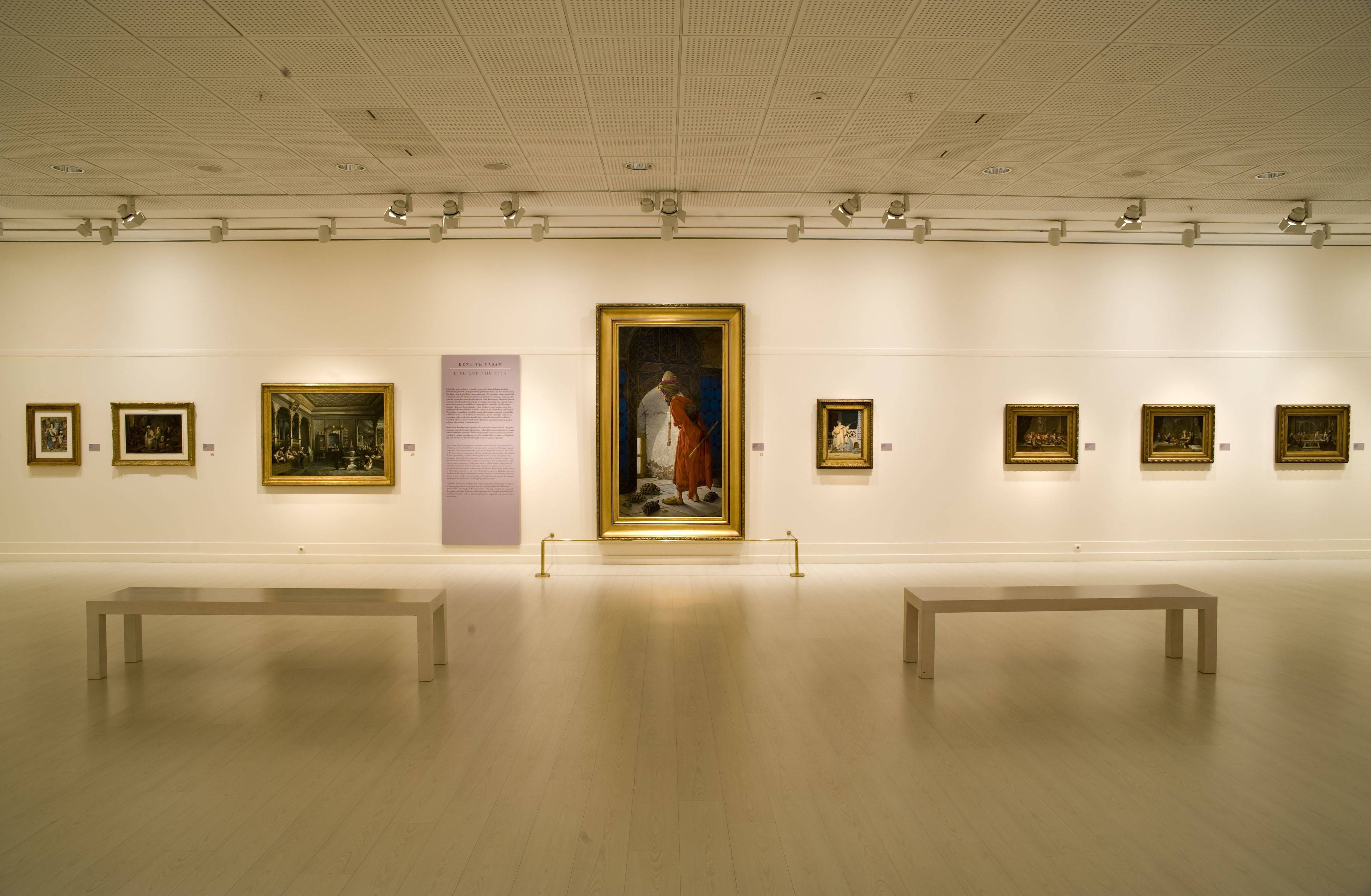 Gallery 桌布 壁紙 — 一個寧靜的藝術畫廊，白色牆壁和木地板，在聚光燈下展示帶框的畫作，並設有長椅供觀眾使用。