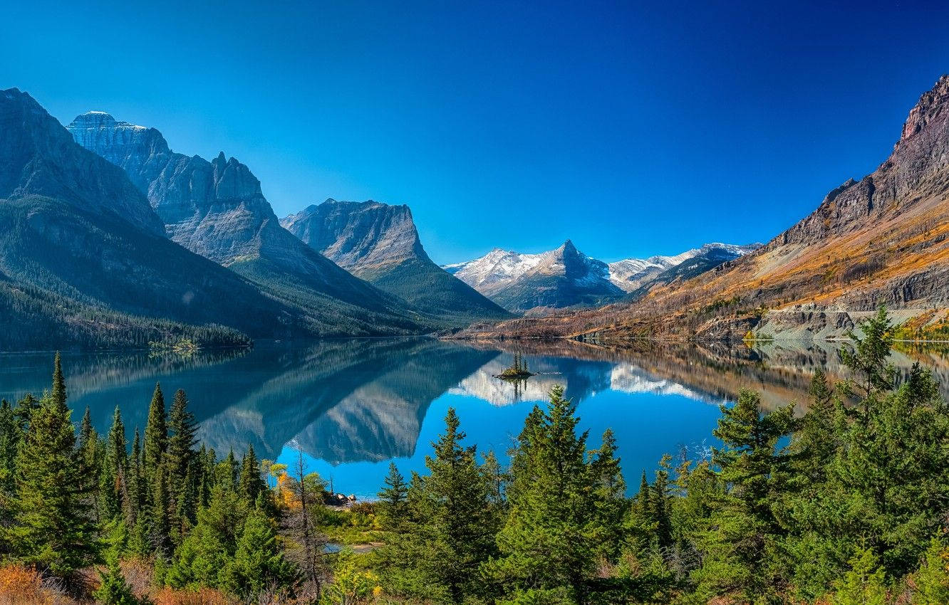 Lake 桌布 壁紙 — 一個寧靜的高山湖泊，在清澈的藍天下映照著白雪覆蓋的山峰和崎嶇的懸崖，四周環繞著常青樹。