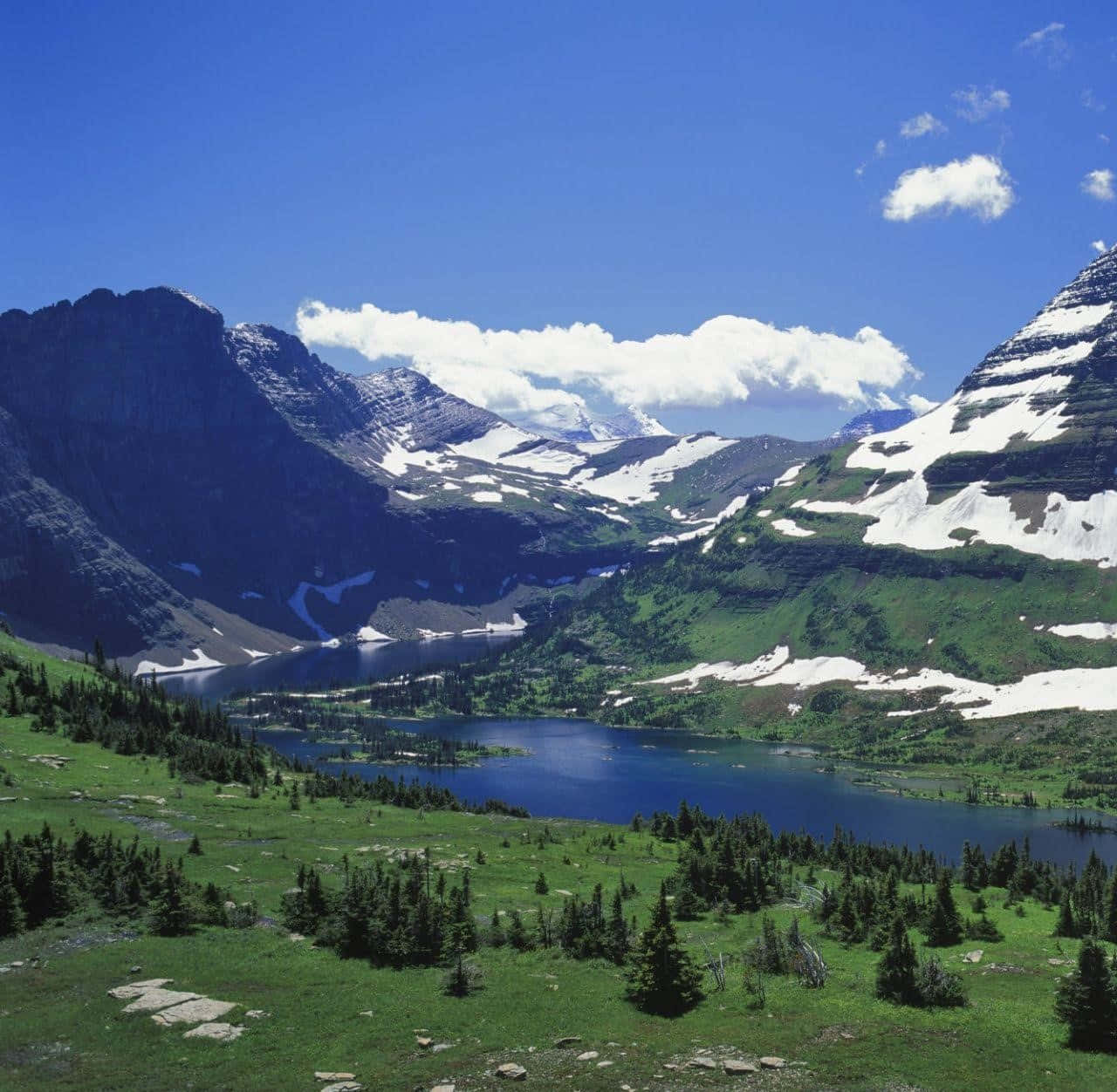 Montana 桌布 壁紙 — 一個寧靜的高山湖泊，坐落在白雪覆蓋的山巒之間，天空湛藍，白雲朵朵。