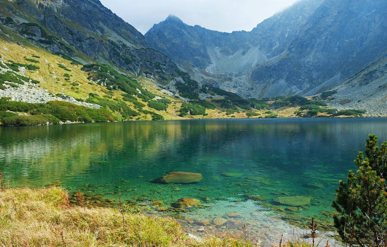 Slovakia 桌布 壁紙 — 一個寧靜的高山湖泊，清澈見底的碧藍湖水，坐落於崎嶇岩石山脈之間，天空柔和。