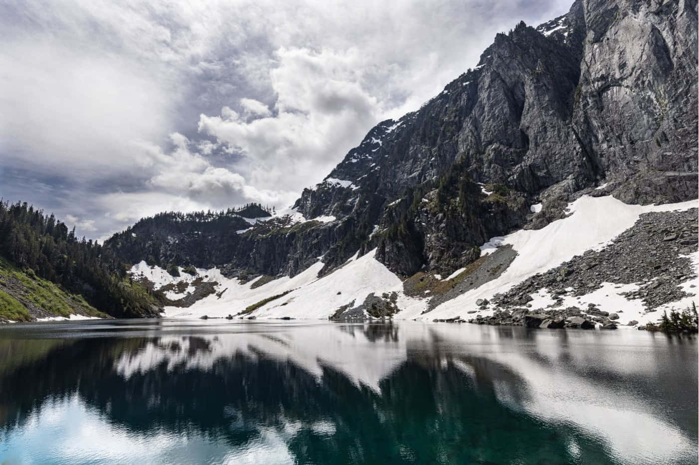 Lake 桌布 壁紙 — 一個寧靜的高山湖泊在陰天之下映照著崎嶇的積雪山脈。