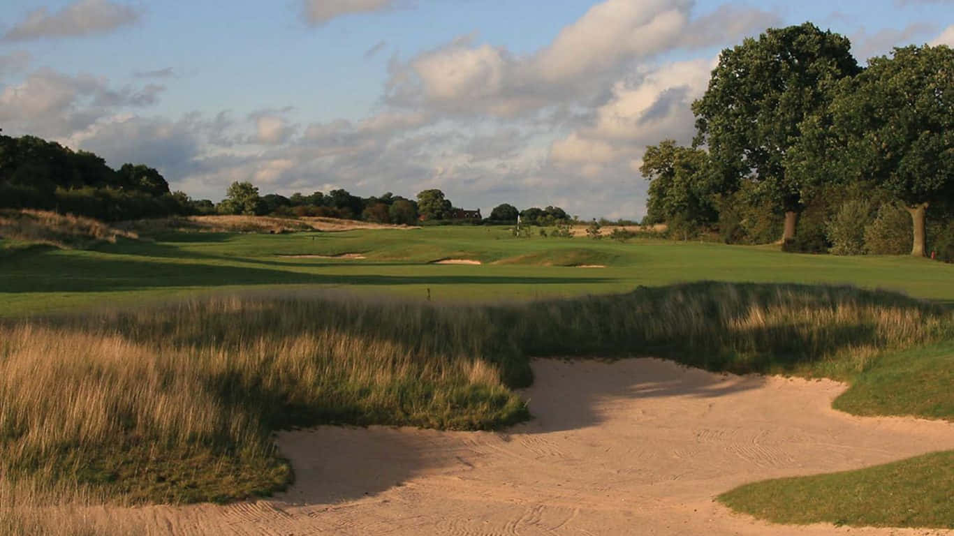 1366x768 Golf Course 桌布 壁紙 — 一個寧靜的高爾夫球場，在日落時分，有茂密的綠色球道、沙坑和高草，天空部分多雲。