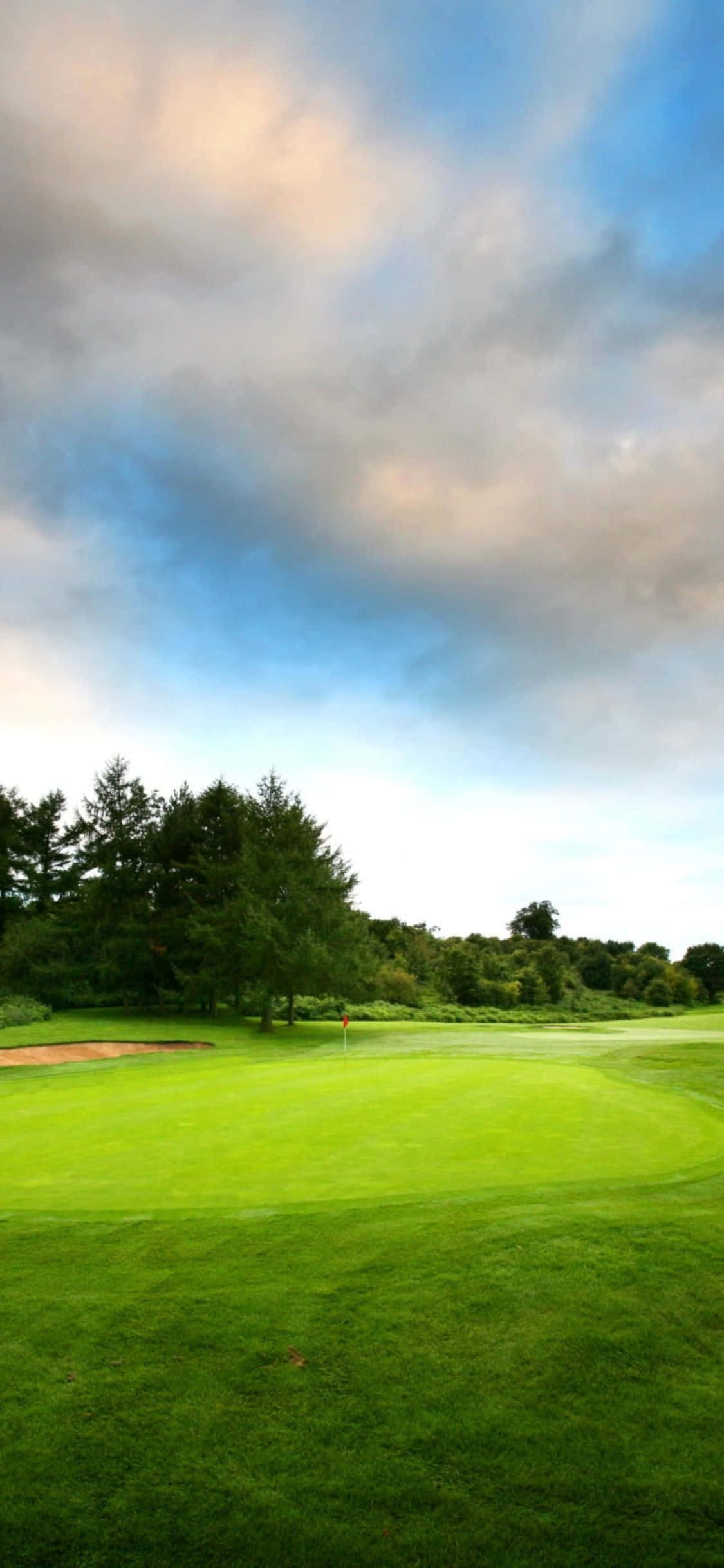 iPhone X Golf Course 桌布 壁紙 — 一個寧靜的高爾夫球場在廣闊的天空下延伸，柔和的雲朵和遠處的樹木勾勒出球道。